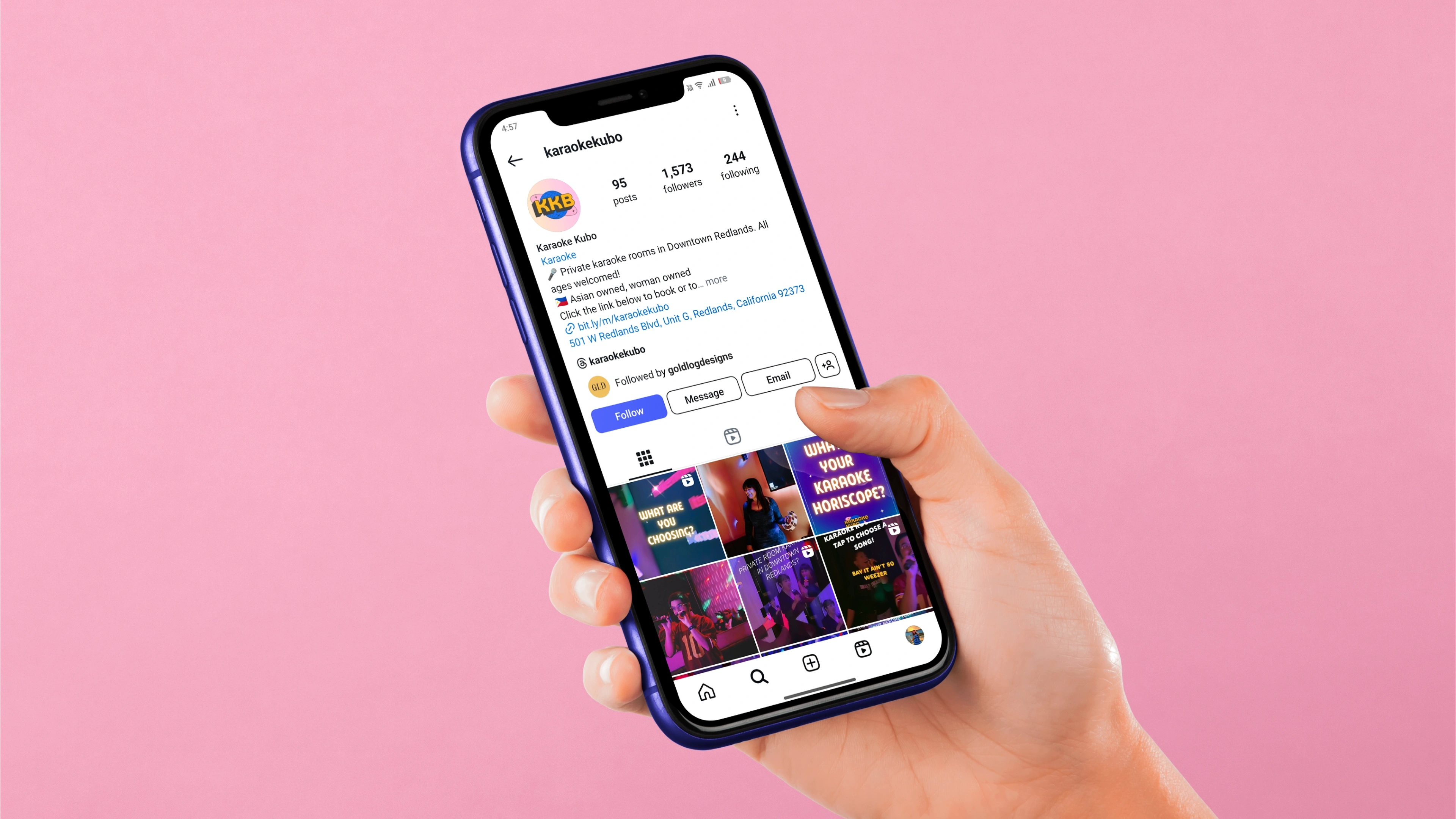 A hand holding a phone showing the Karaoke Kubo Instagram profile, set on a soft pink ground