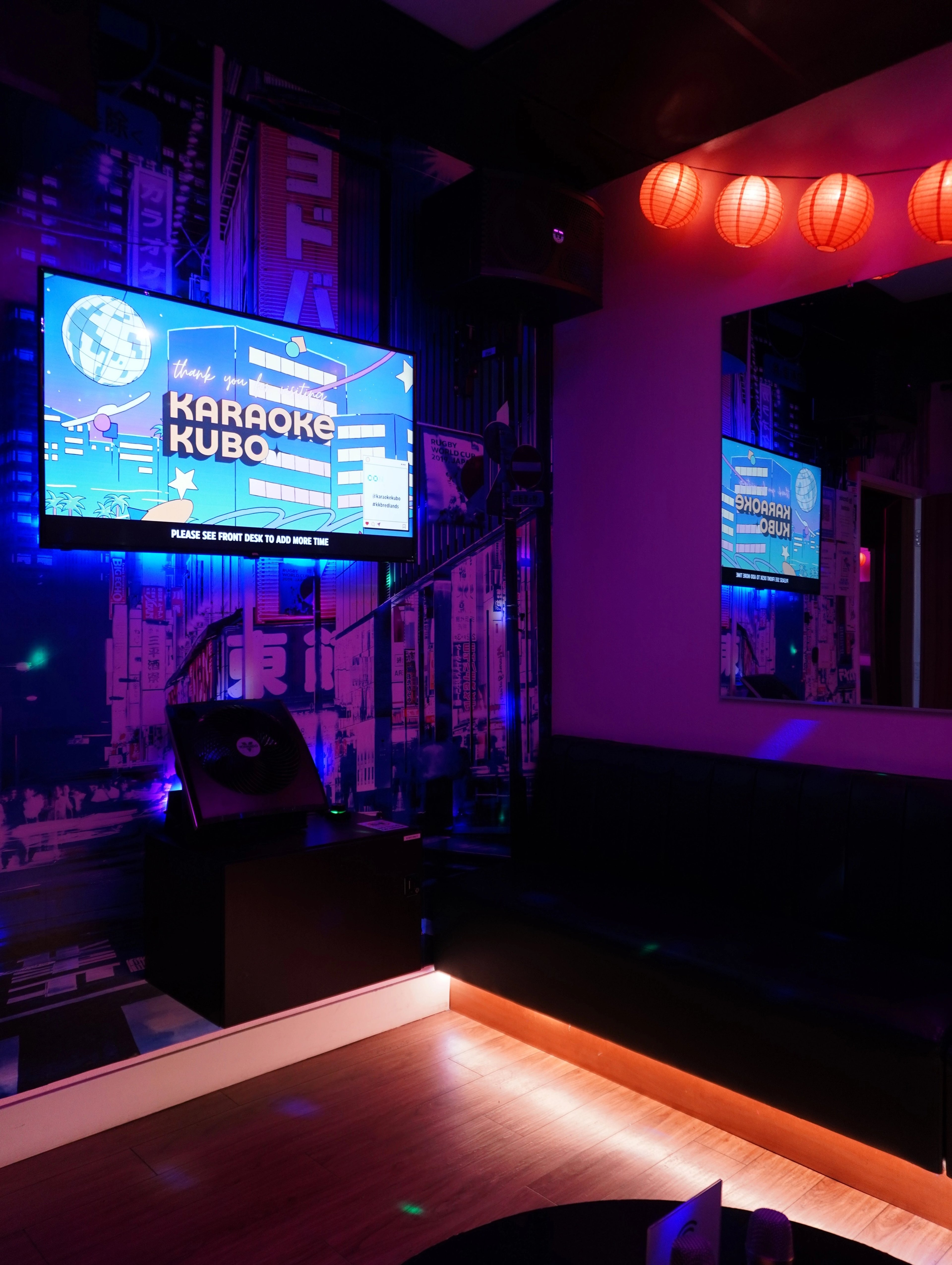 Inside a Karaoke Kubo private room — the wordmark on screen, neon light and red lanterns