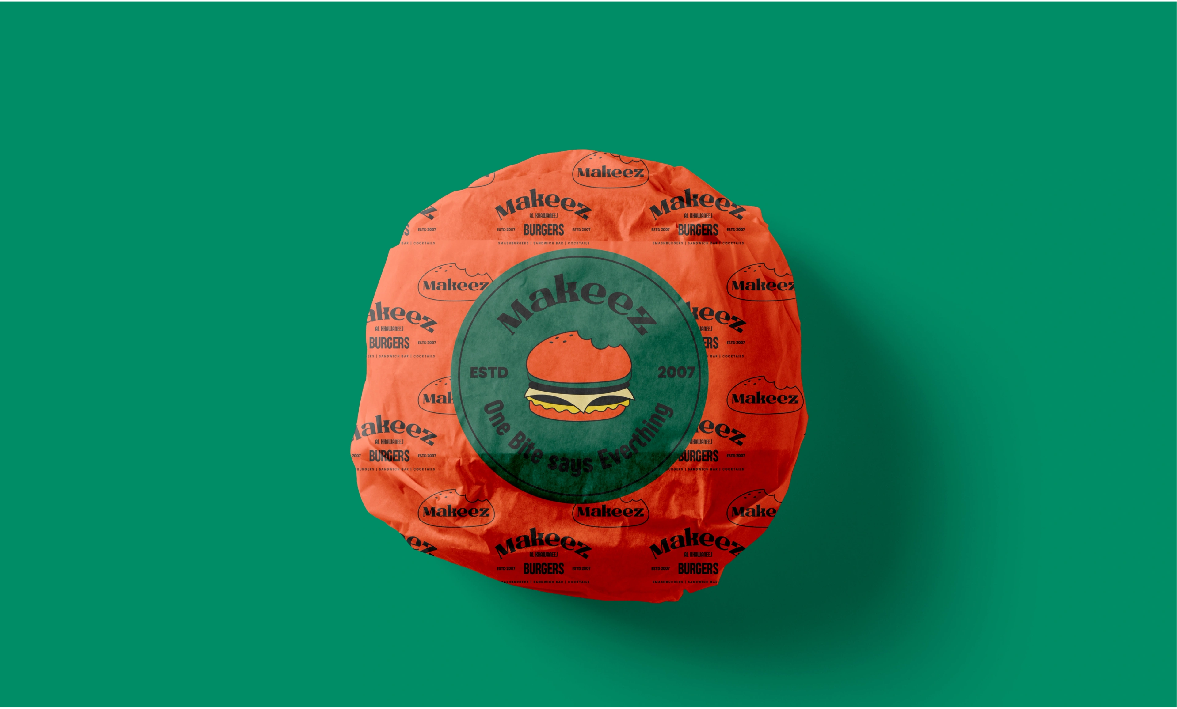 A Makeez burger wrapped in branded orange paper with a green seal