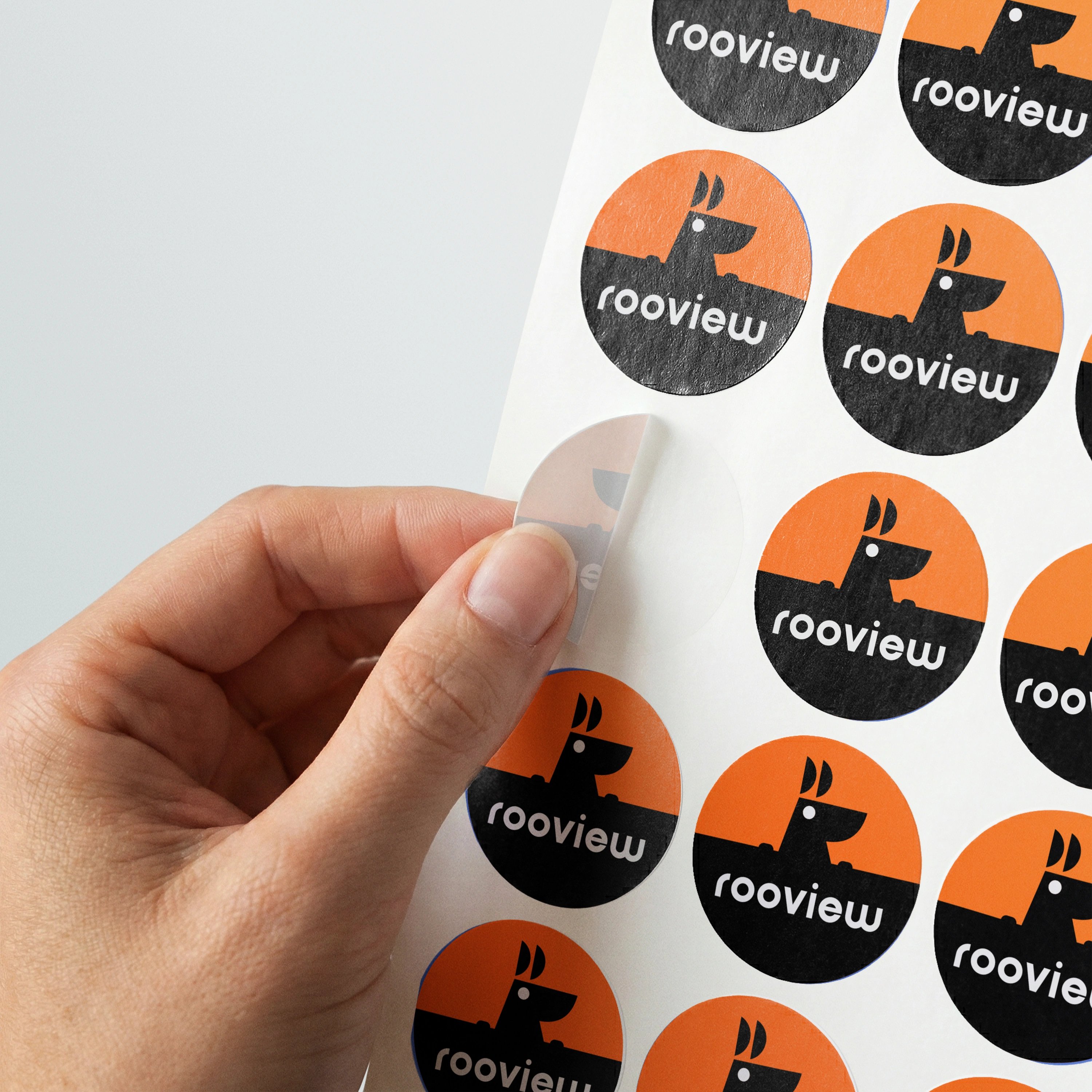 a hand peeling a round RooView kangaroo sticker from a printed label sheet