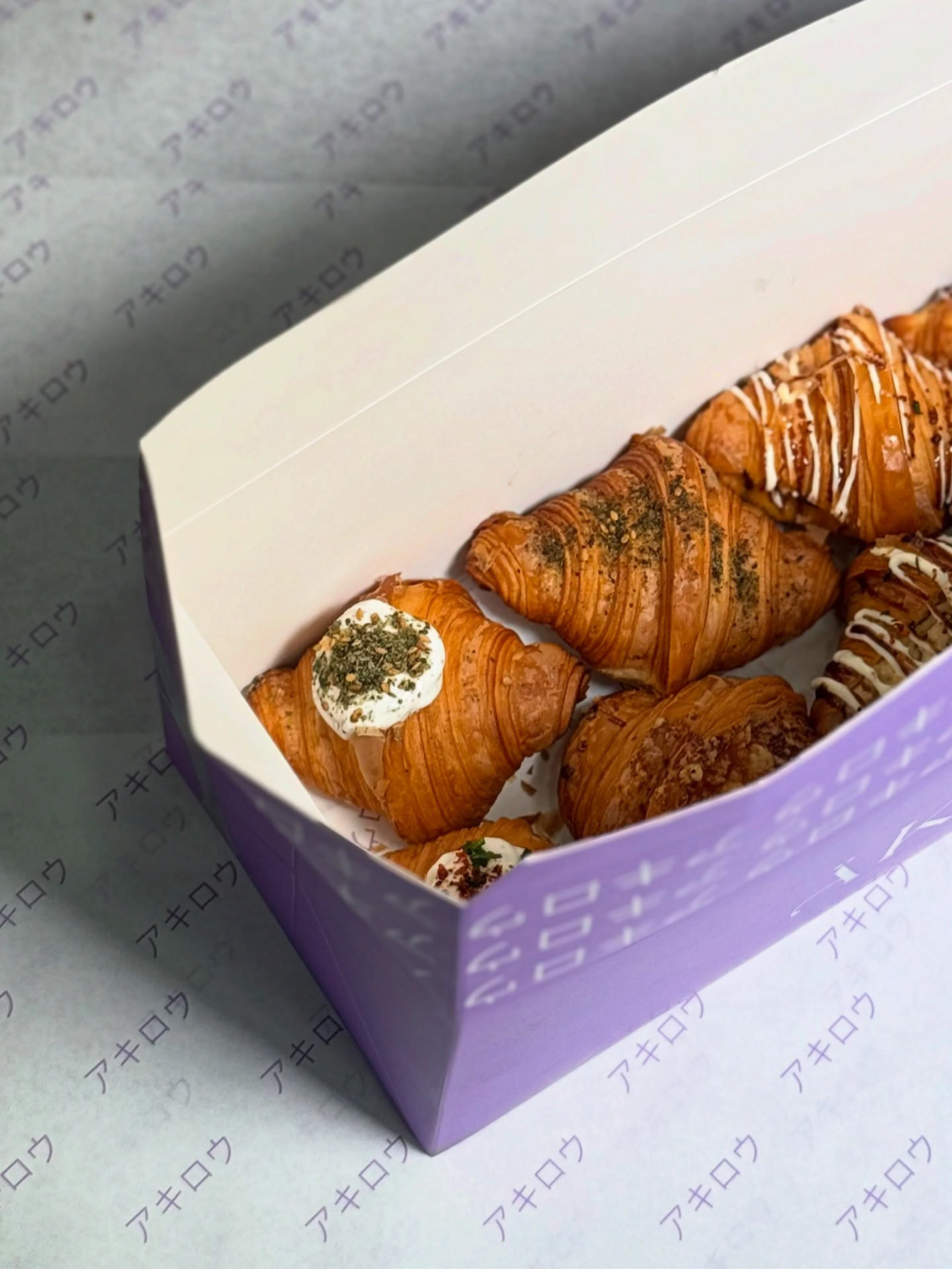Open purple ÄKIRO pastry box filled with glazed croissants