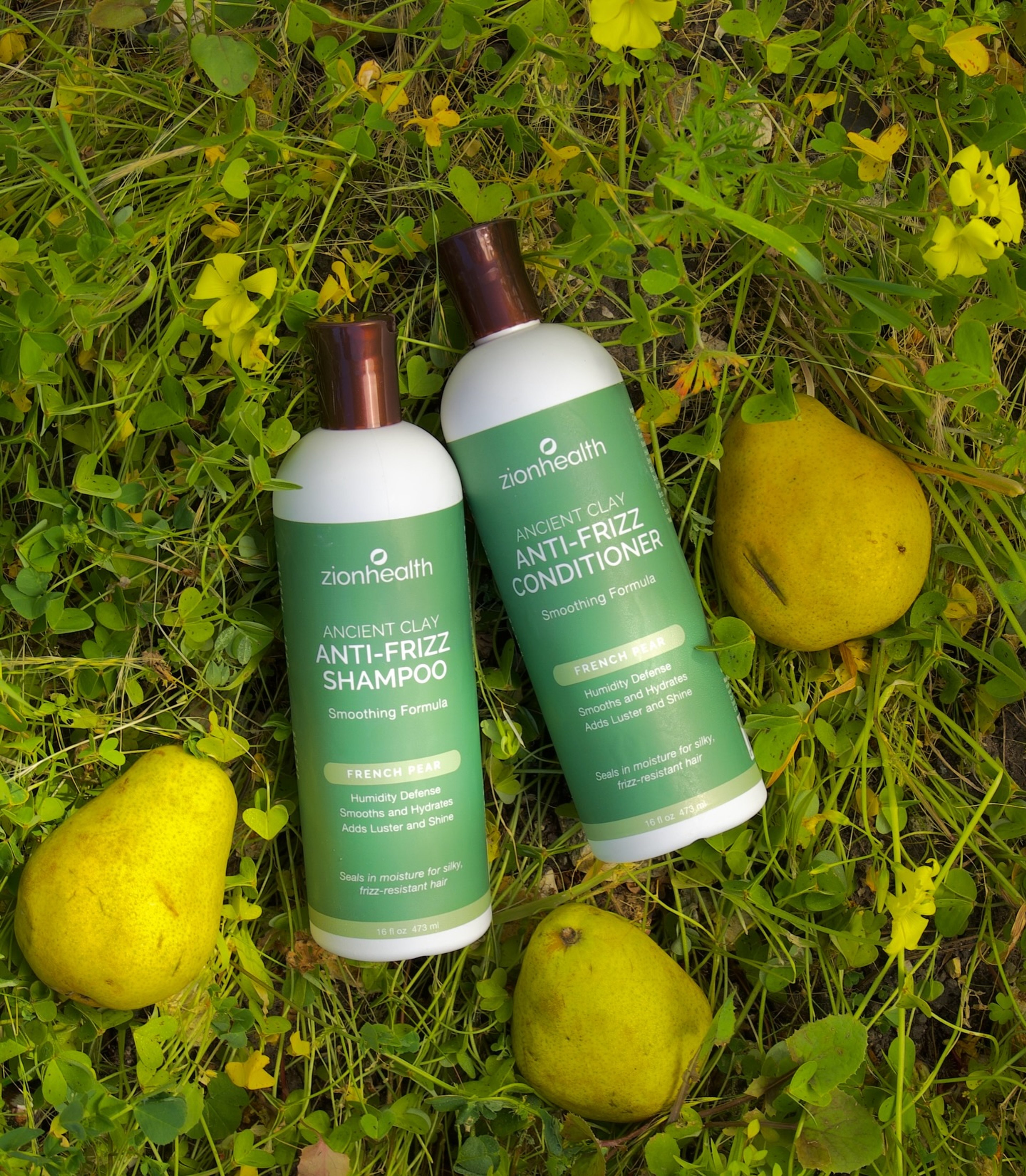 Zion Health Ancient Clay anti-frizz shampoo and conditioner bottles resting in grass among yellow pears