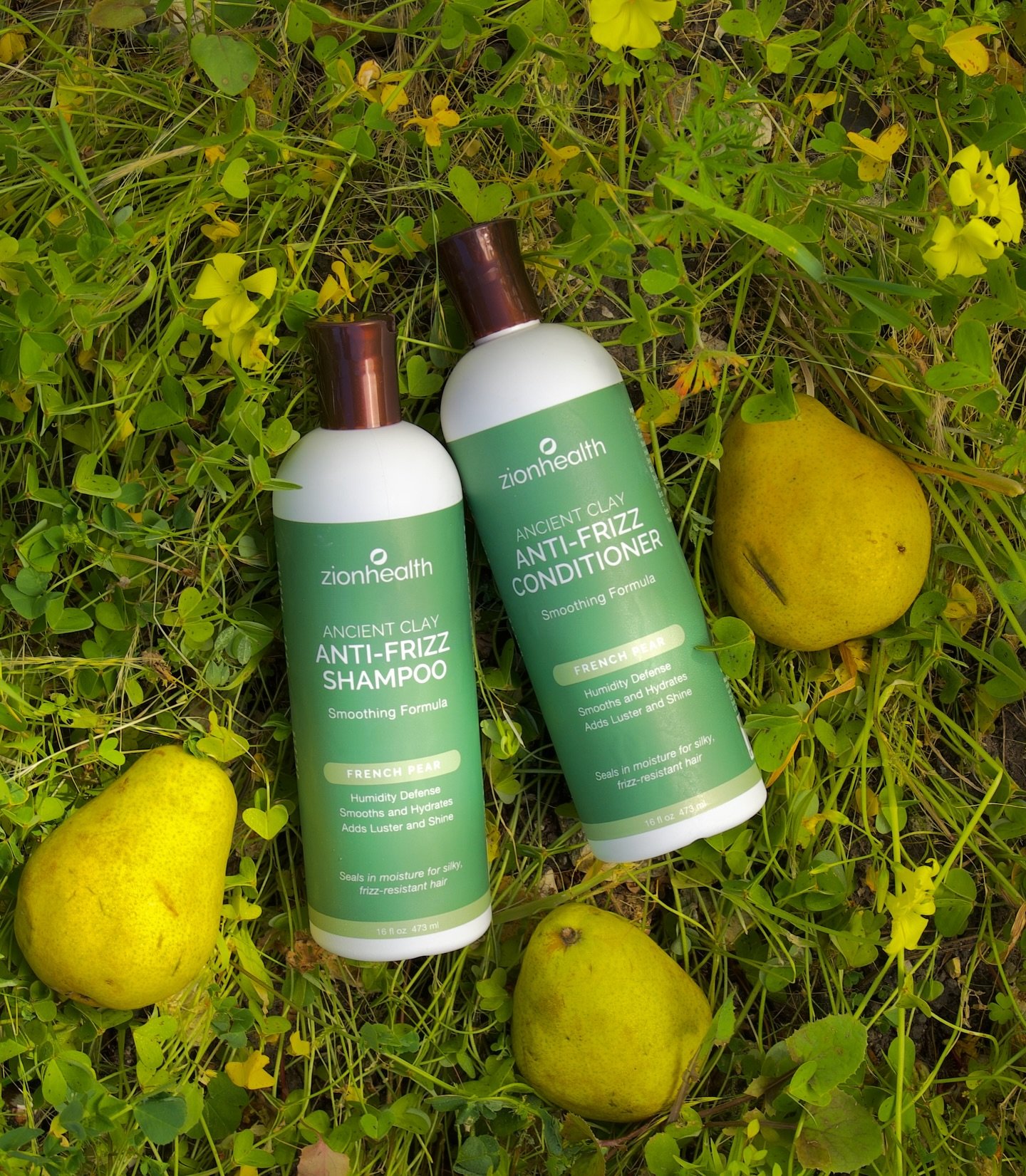 Zion Health Ancient Clay anti-frizz shampoo and conditioner bottles resting in grass among yellow pears
