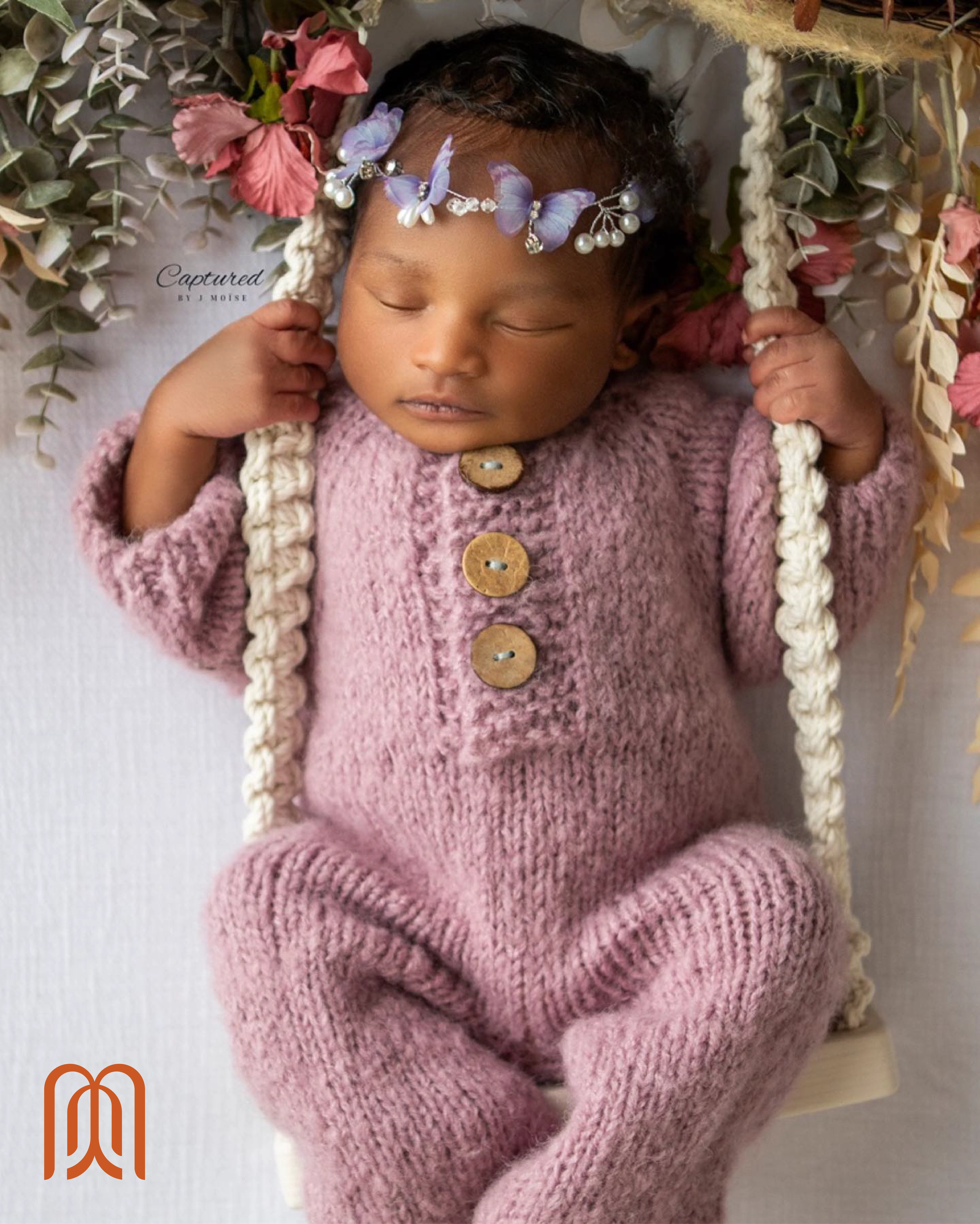 a newborn in a pink knit outfit nestled among flowers and soft fabric