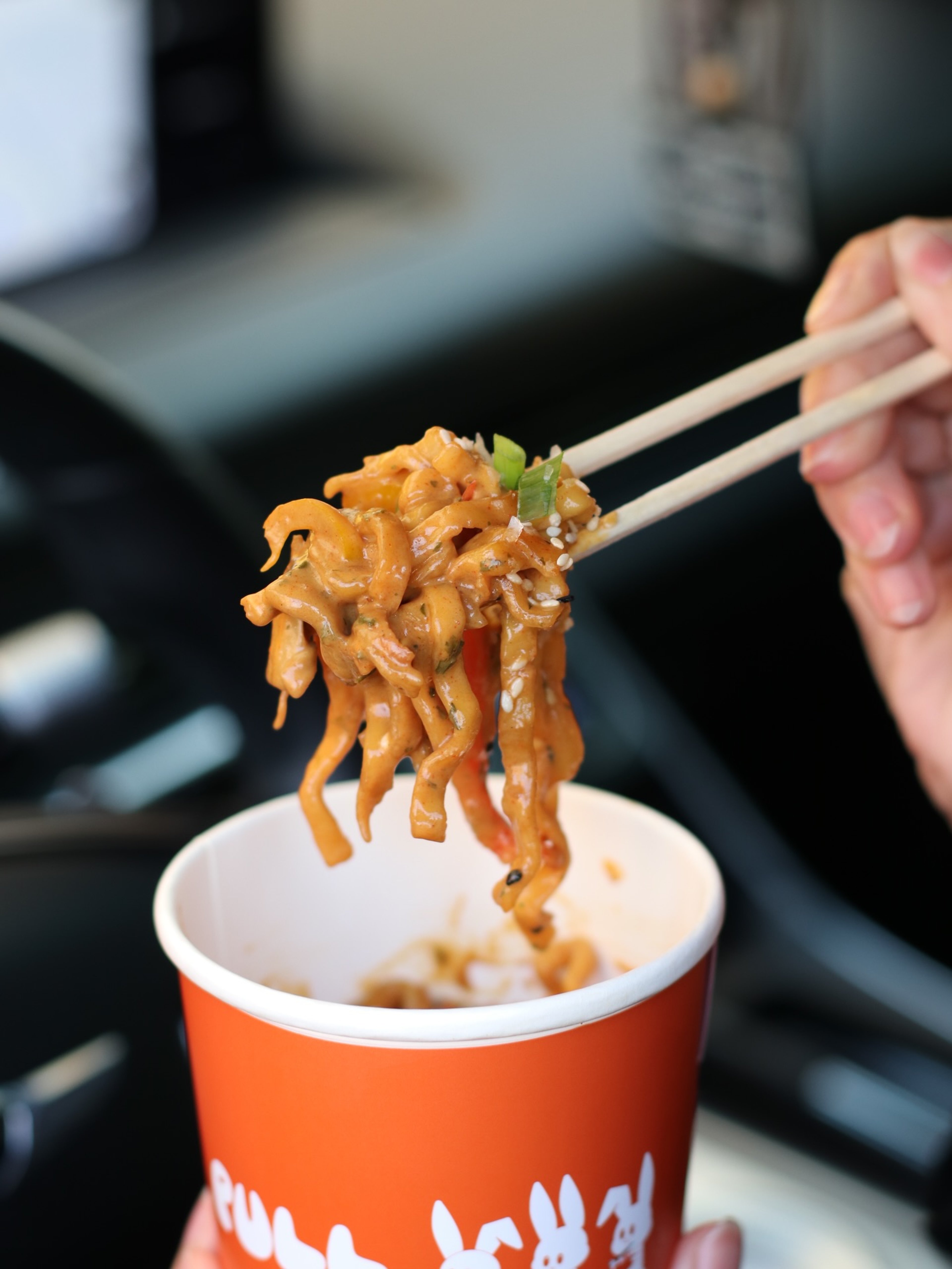 Chopsticks lifting saucy PULL noodles from the orange bunny-print cup
