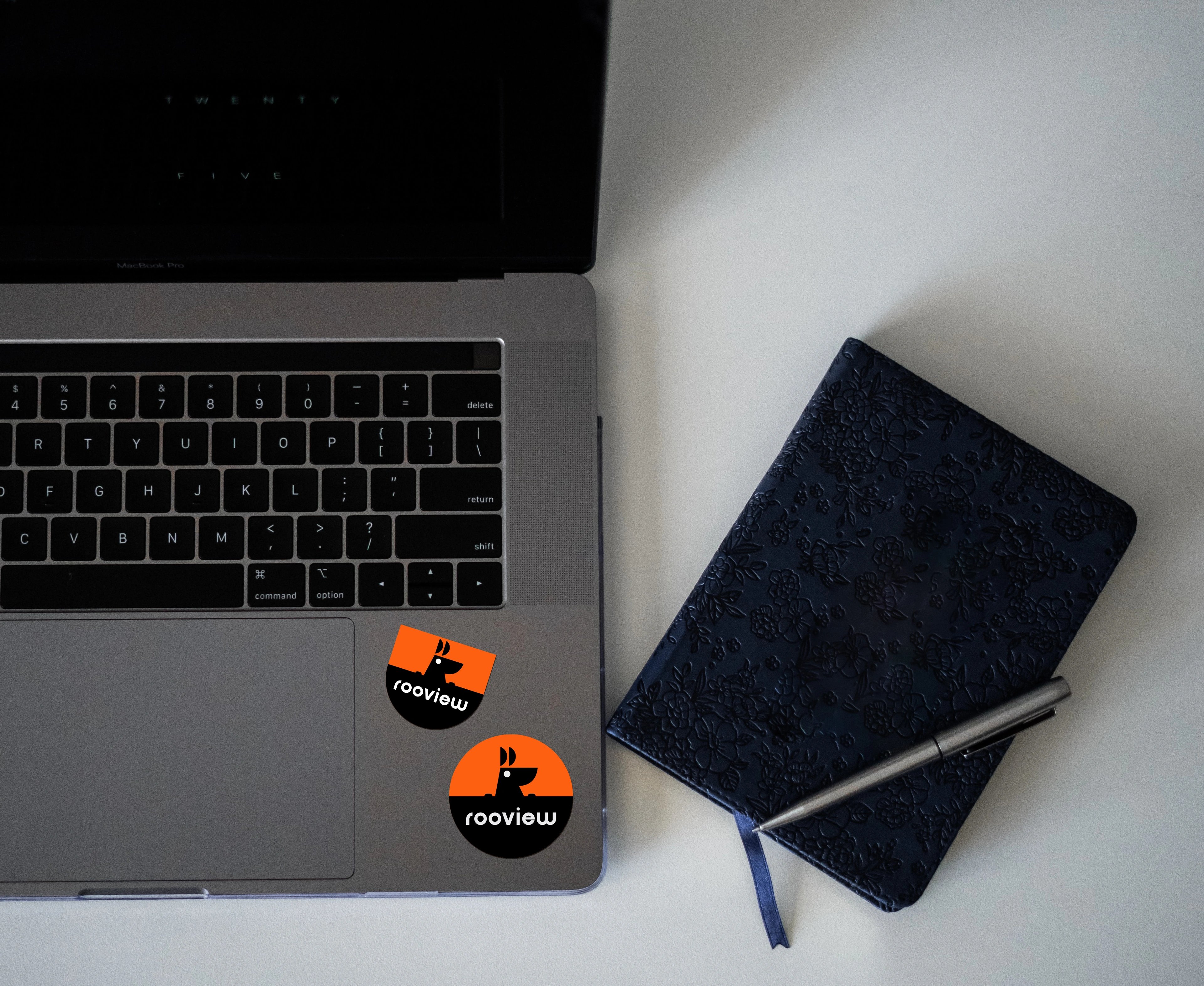RooView kangaroo stickers on a MacBook beside a navy notebook and pen