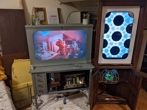 Two screens with in  a grey cabinet and a tall corner cabinet.