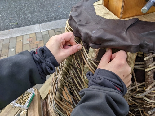 Hands tying leather onto wooden pole