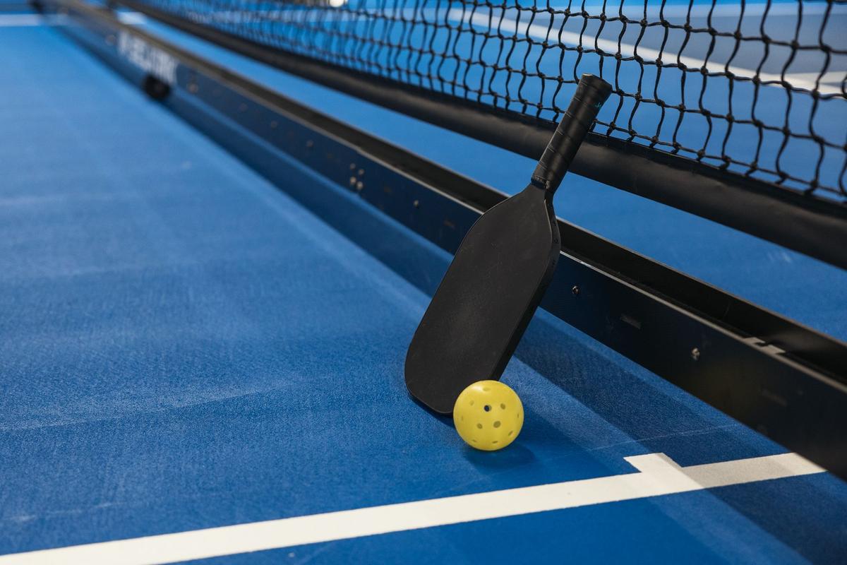 A portable pickleball net on a blue court, with a paddle and yellow holed ball resting against its frame