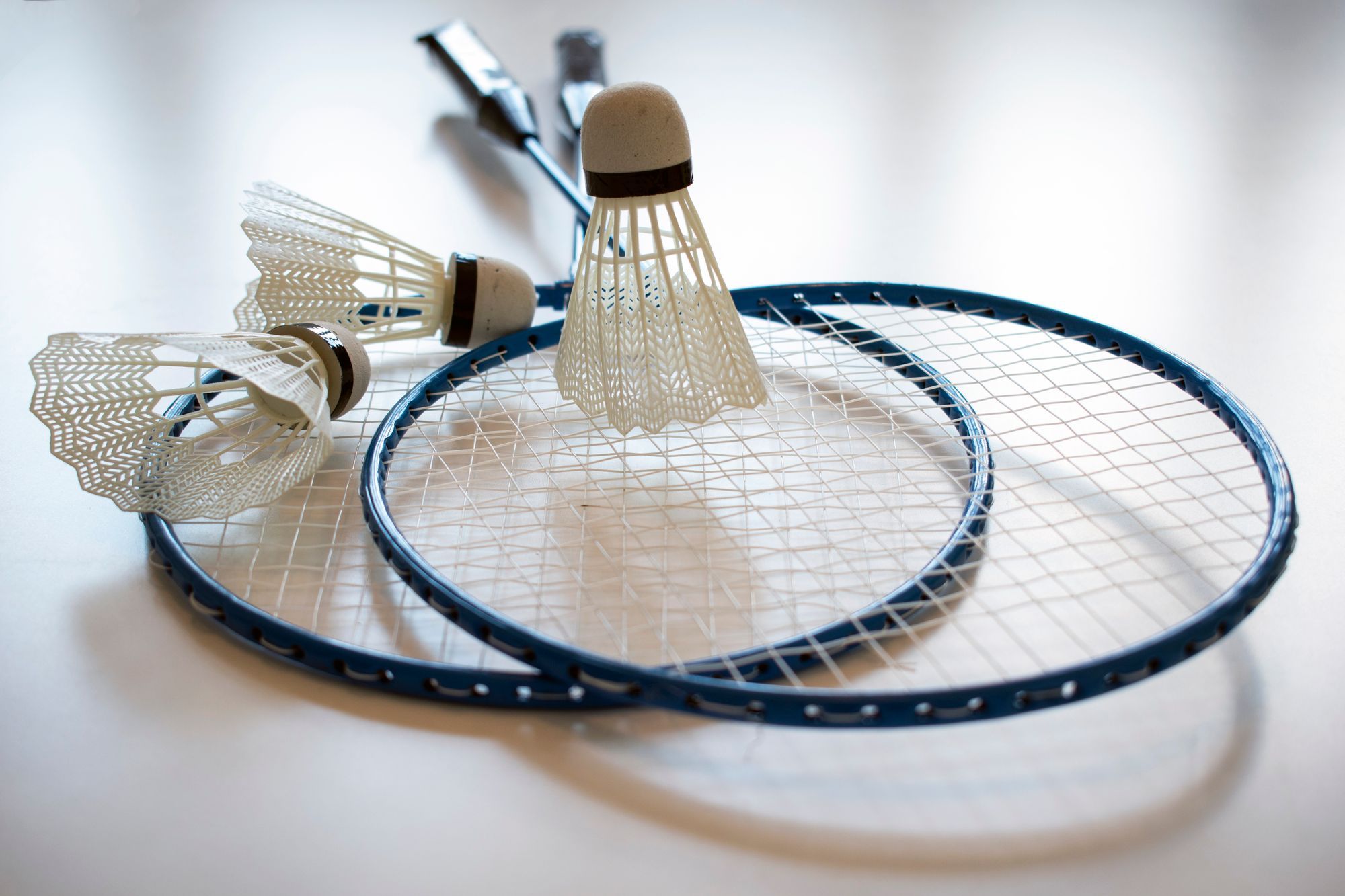 Two badminton rackets lying crossed on a pale surface with three plastic shuttlecocks on and beside them