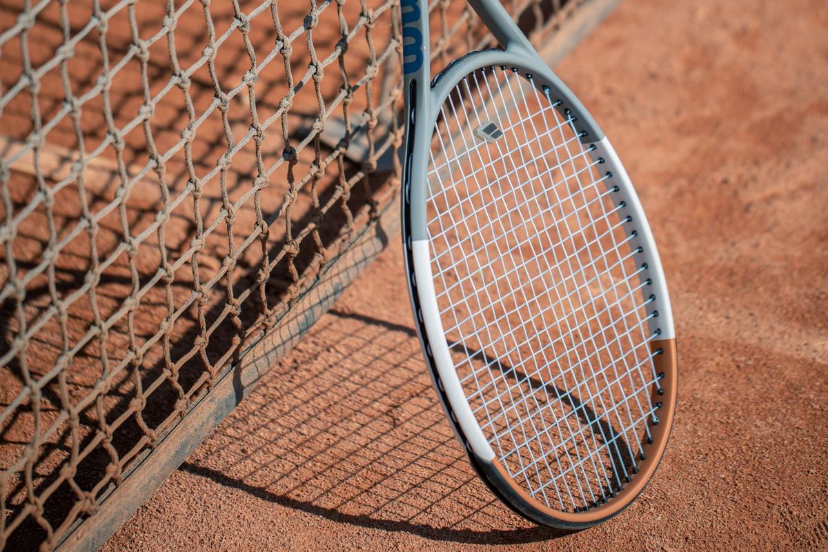 A strung tennis racket leaning against the net on an outdoor clay court