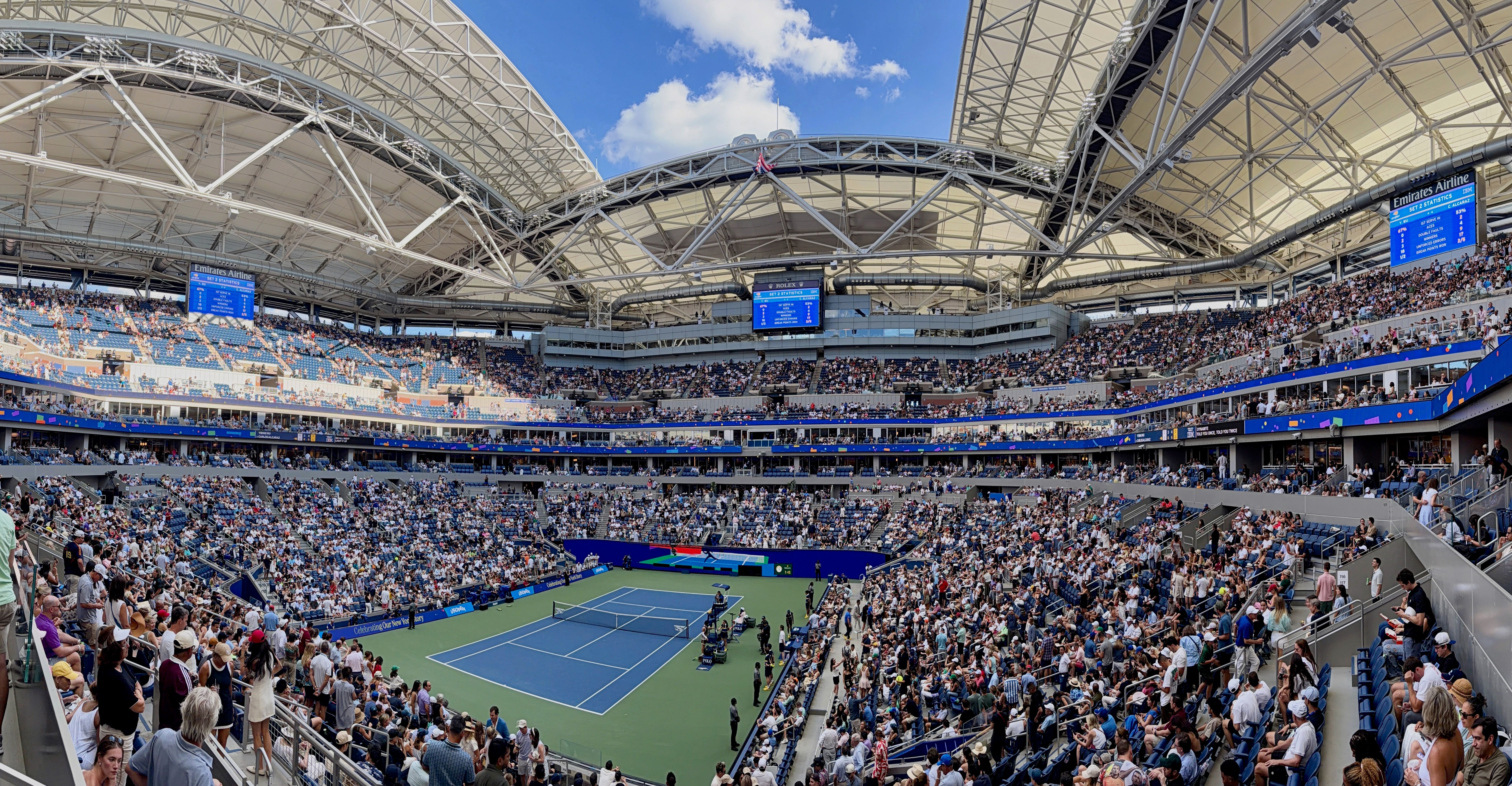 Panorama of a crowded Arthur Ashe Stadium during a match, with the roof open