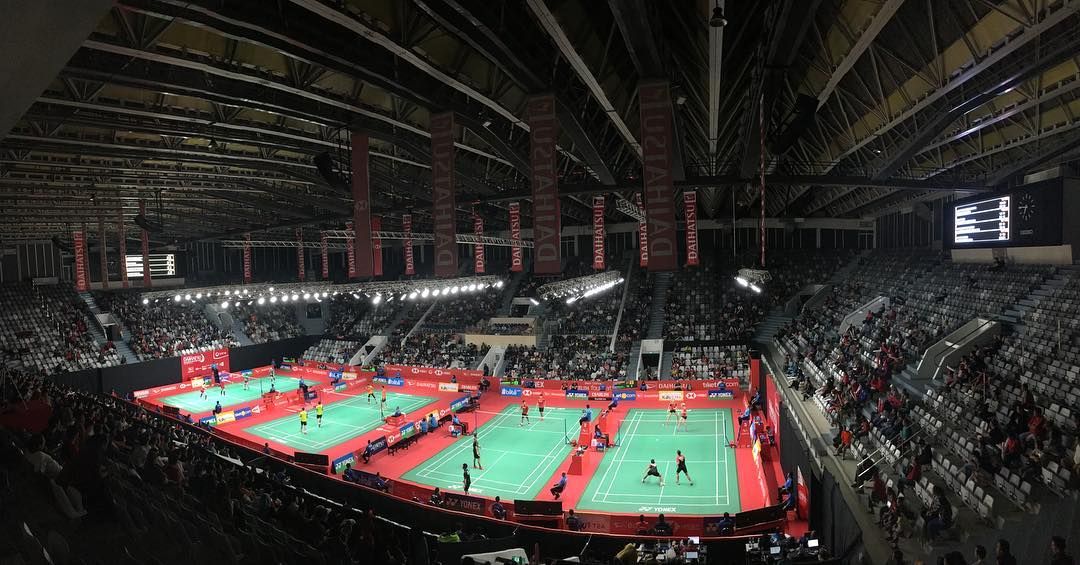 Badminton matches on several courts inside Istora Senayan, with spectators in the stands