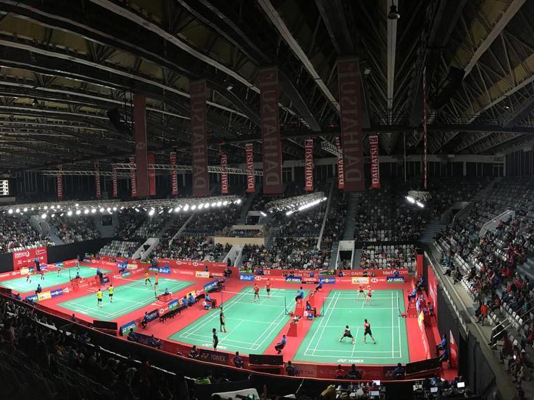 Badminton matches on several courts inside Istora Senayan, with spectators in the stands