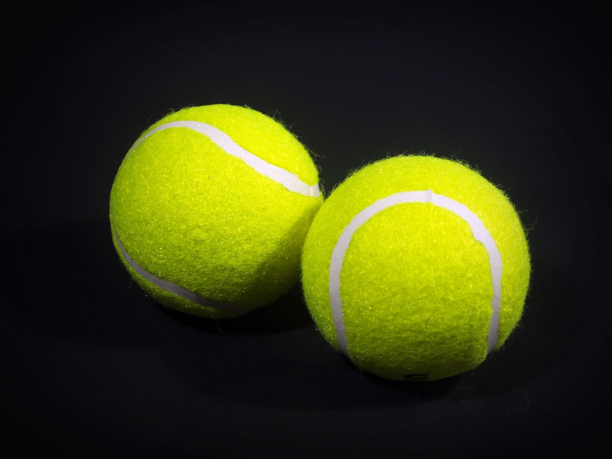 Two optic-yellow felt tennis balls with white seams on a black background