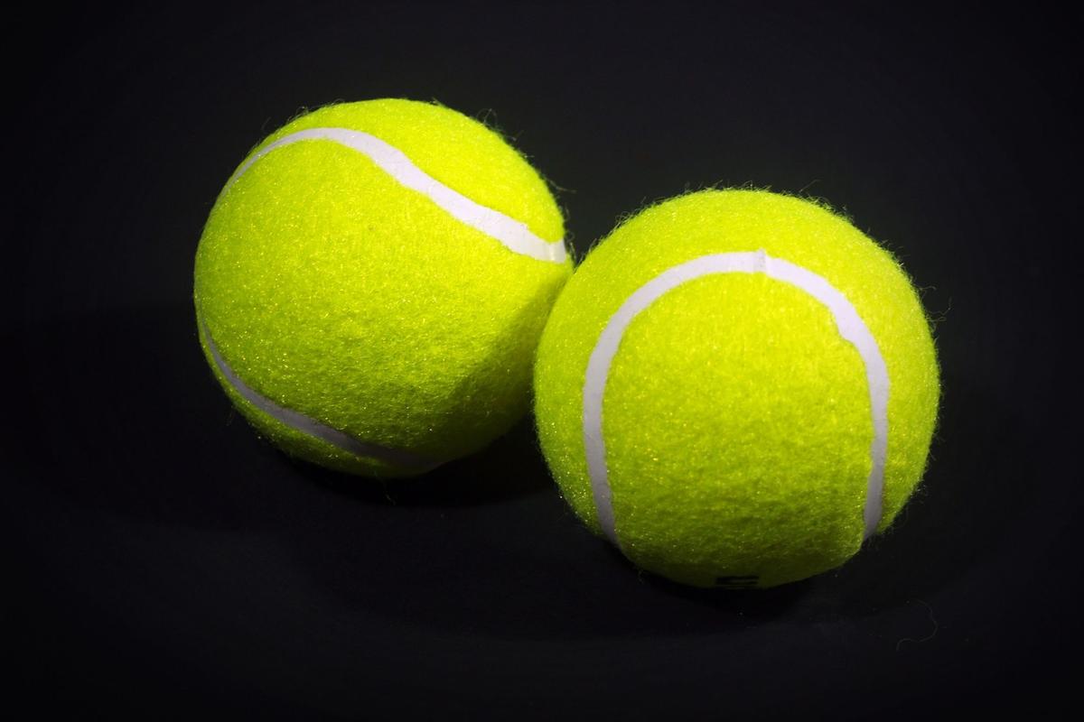 Two optic-yellow felt tennis balls with white seams on a black background
