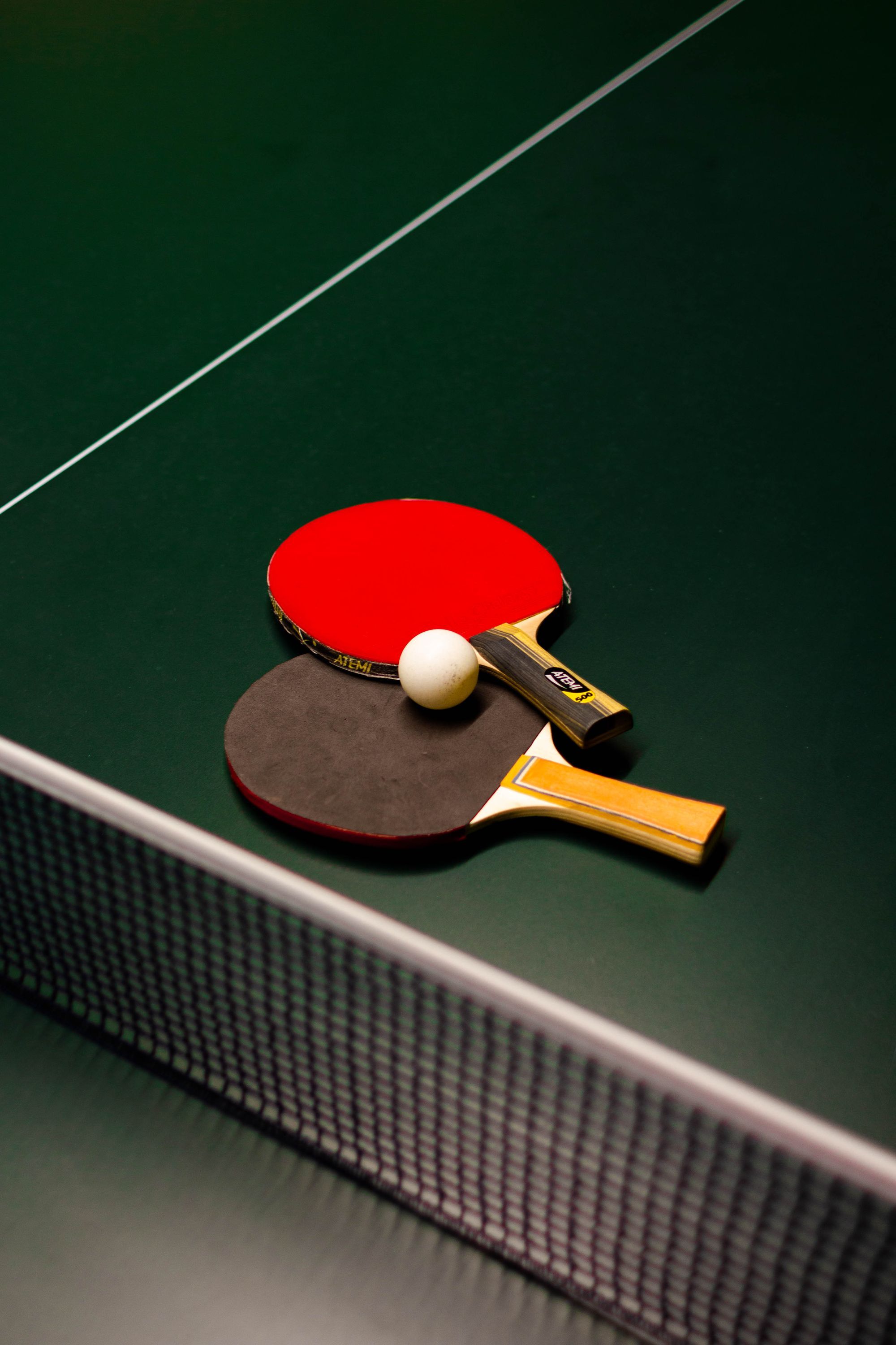 The net across a green table tennis table, with two bats and a white ball lying beside it