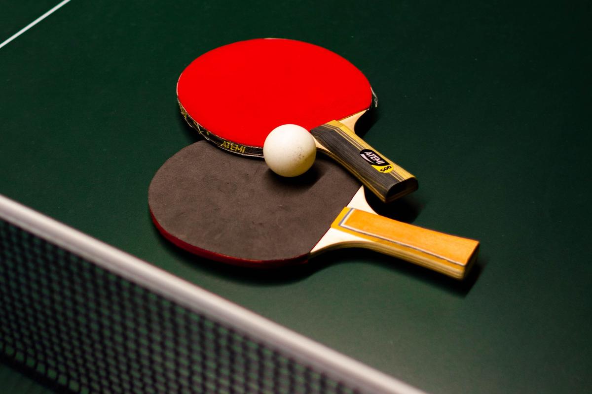 The net across a green table tennis table, with two bats and a white ball lying beside it