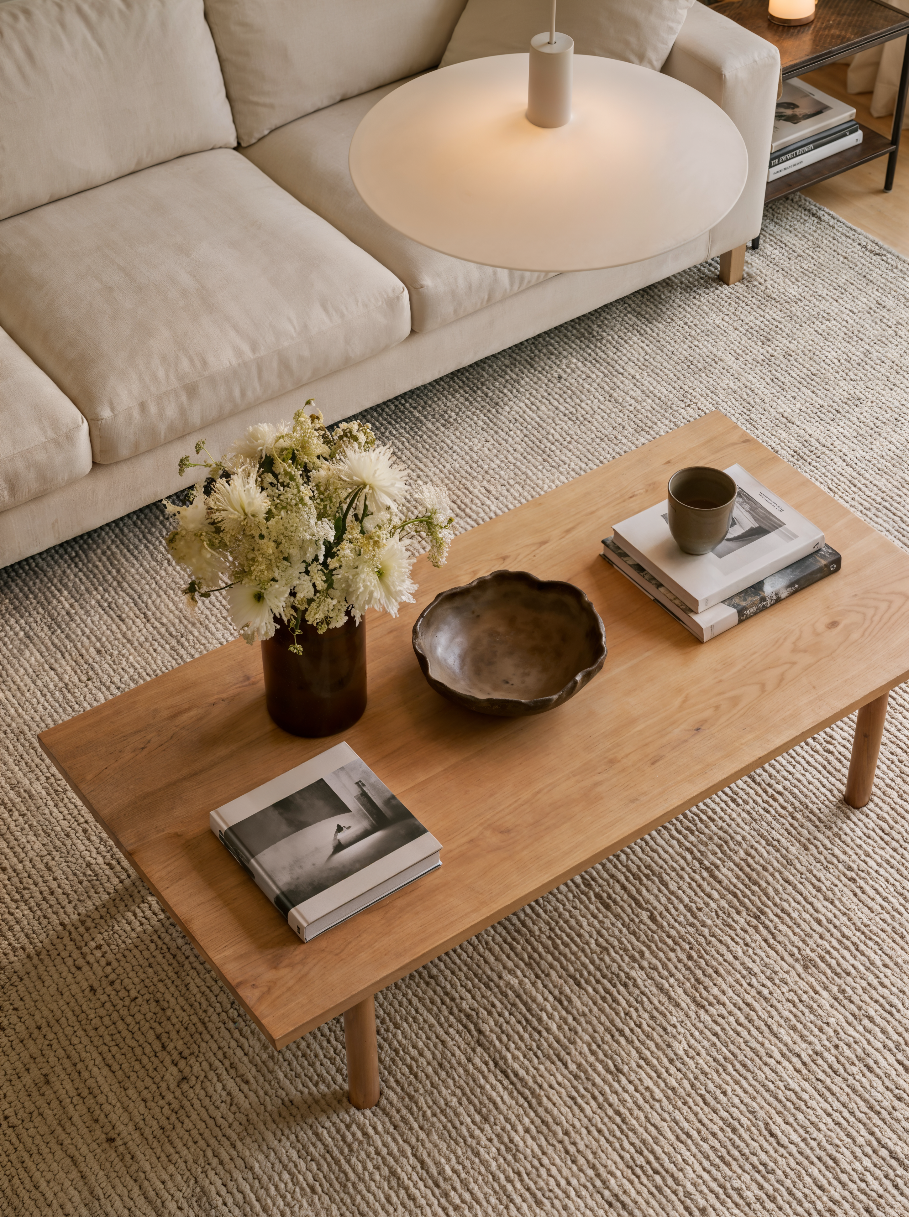 Overhead view of an oak coffee table with books and a ceramic bowl on a woven rug