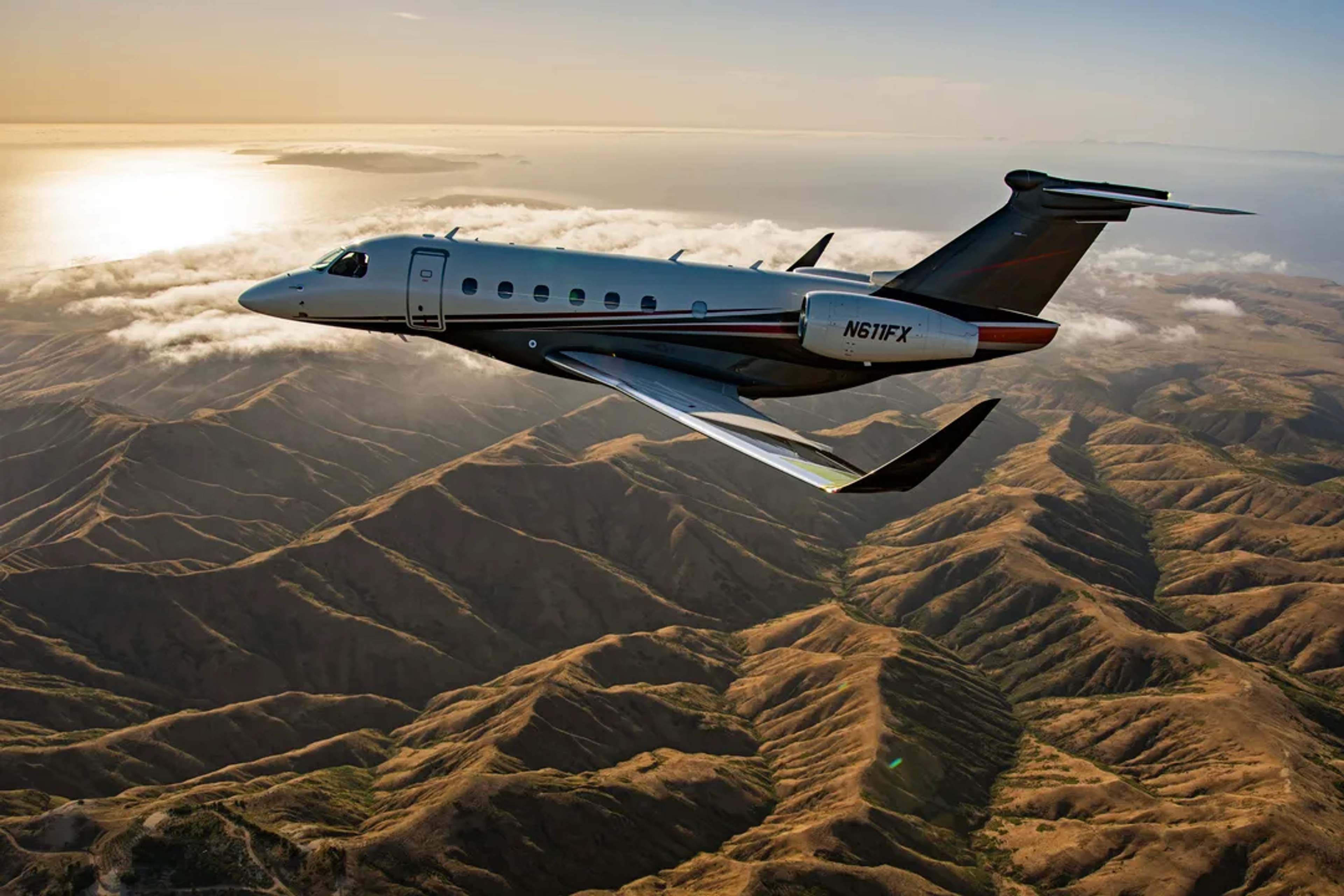 Embraer Praetor 600E in Flexjet livery flying above mountain ridges and low cloud.