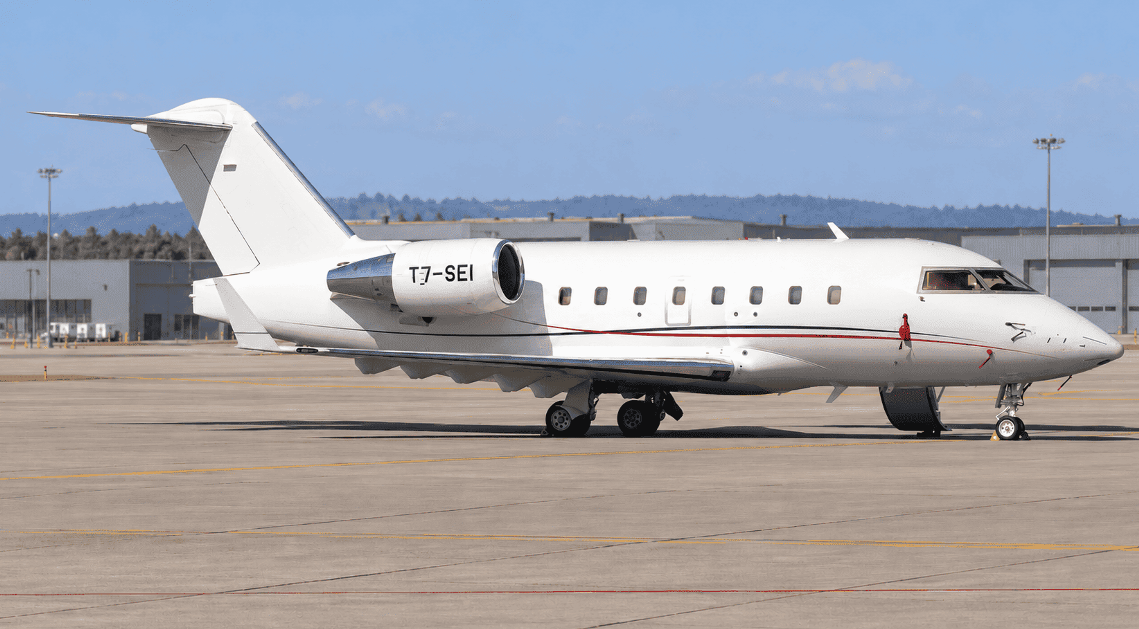 White Bombardier Challenger 604 T7-SEI parked on an airport apron with hangars in the edited background