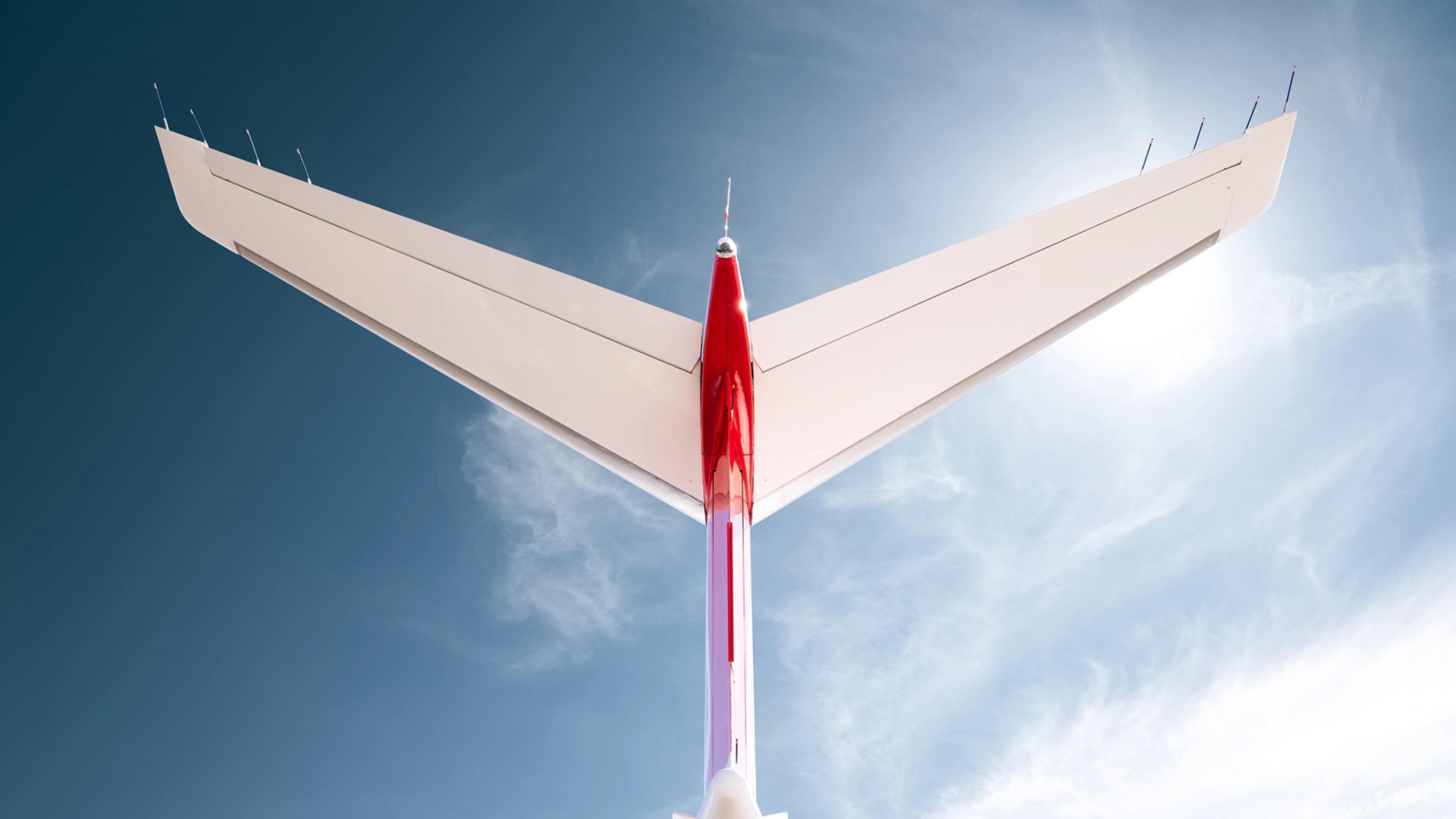 Underside view of a SyberJet SJ30’s swept wing against a blue sky.
