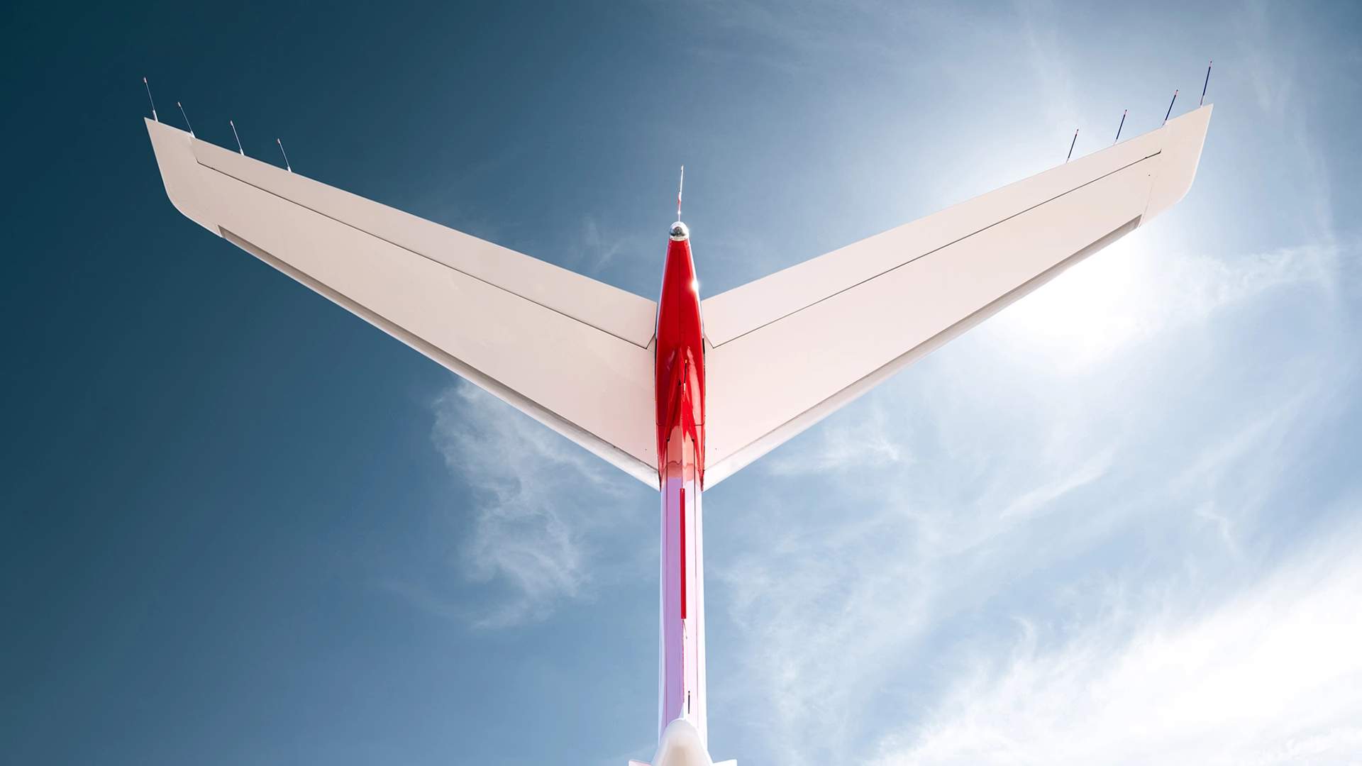 Underside view of a SyberJet SJ30’s swept wing against a blue sky.