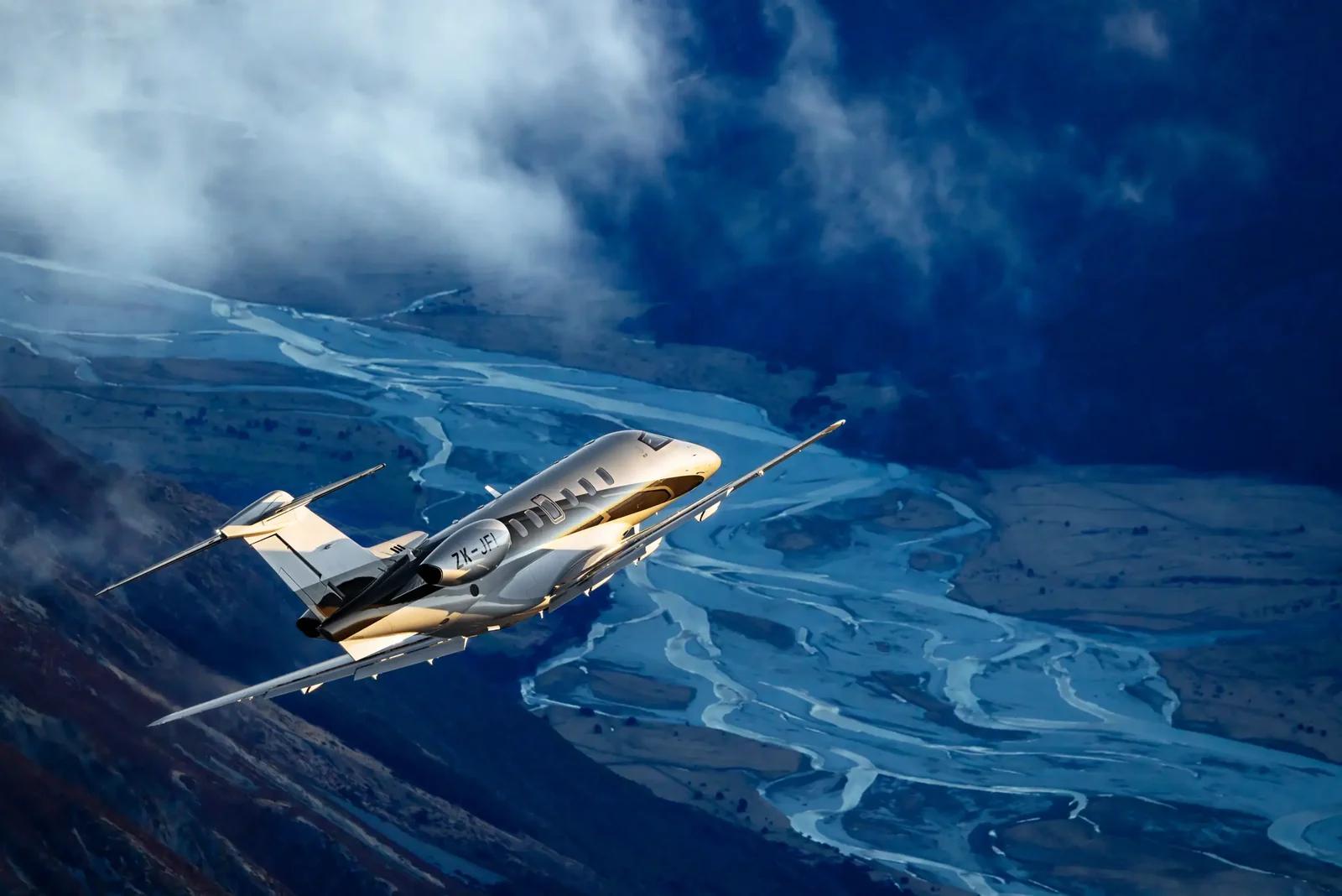 Pilatus PC-24 business jet flying above a braided river valley