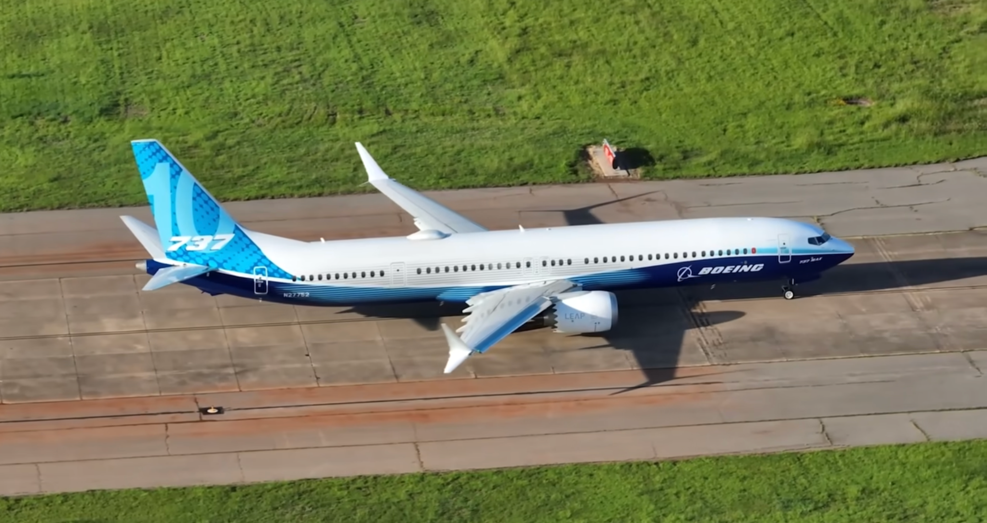 Boeing 737-10 in blue and white manufacturer livery taxiing beside a grass airfield