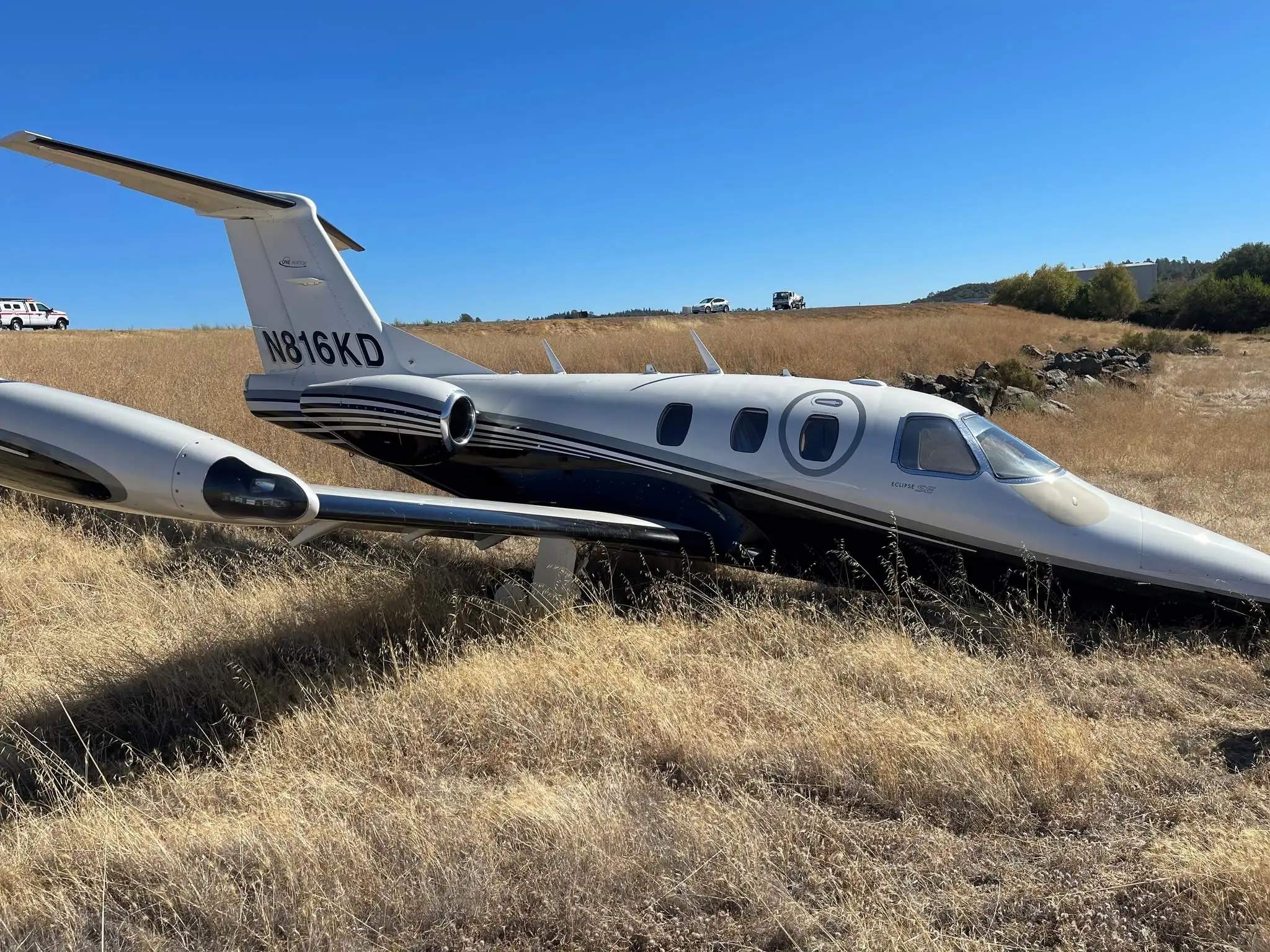 Eclipse 500 N816KD resting in dry grass beyond the runway at Auburn Municipal Airport.