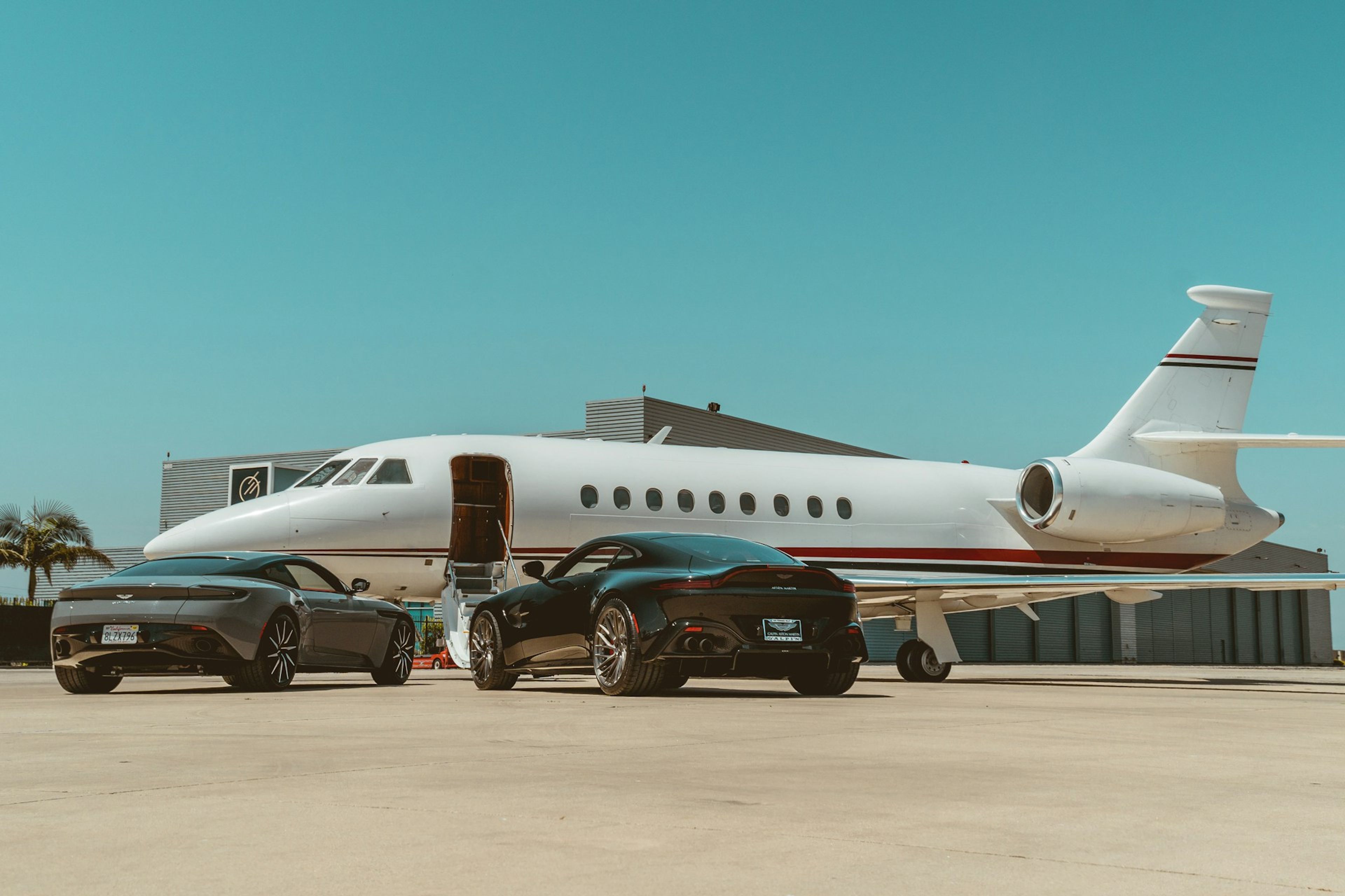 An unbranded business jet parked at a ramp with luxury cars besides it