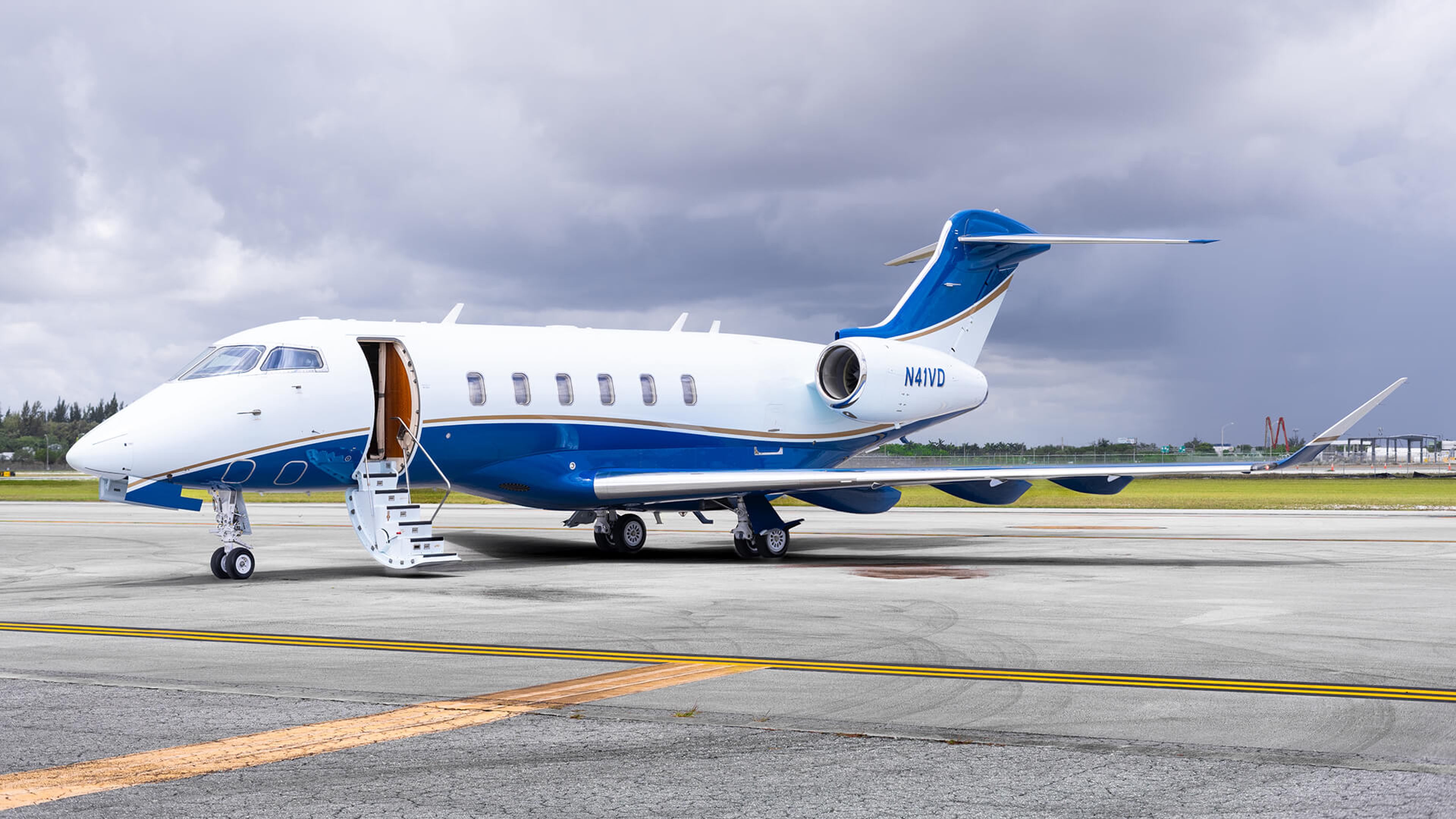 A Bombardier Challenger 350 parked on an airport apron with its cabin door open beneath overcast skies.