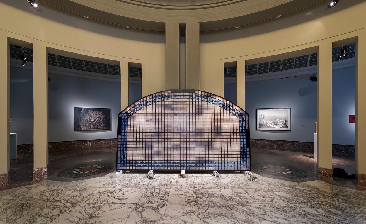 The main exhibition hall featuring works hanged on walls and a paper/plexiglass/aluminum work is installed in the middle of the room.