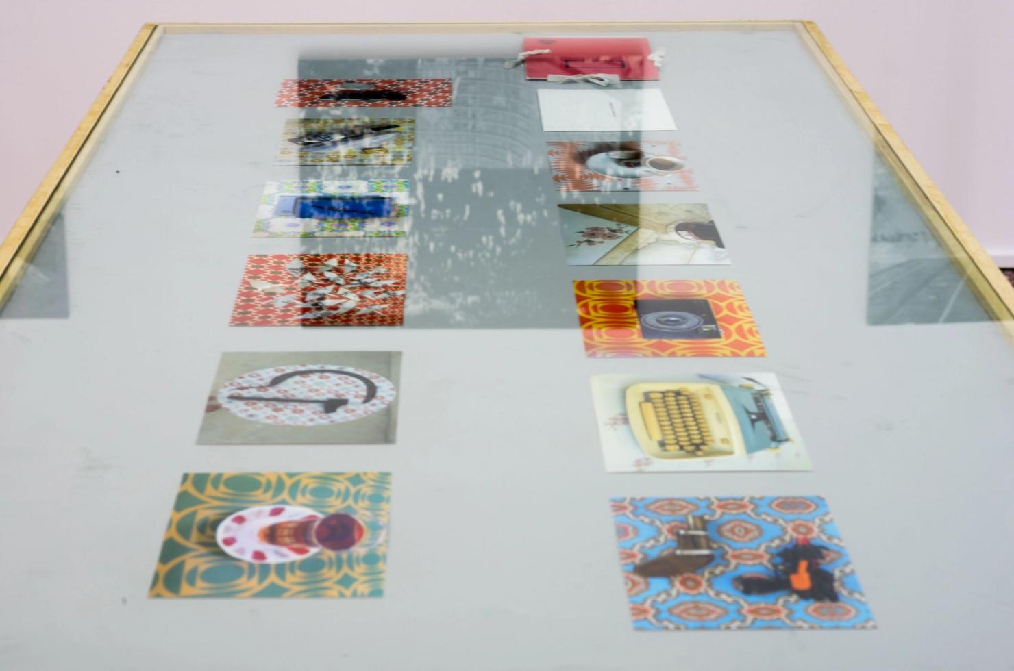 Α thin showcase on a table including different prints depicting objects set against domestic backdrops of an earlier time