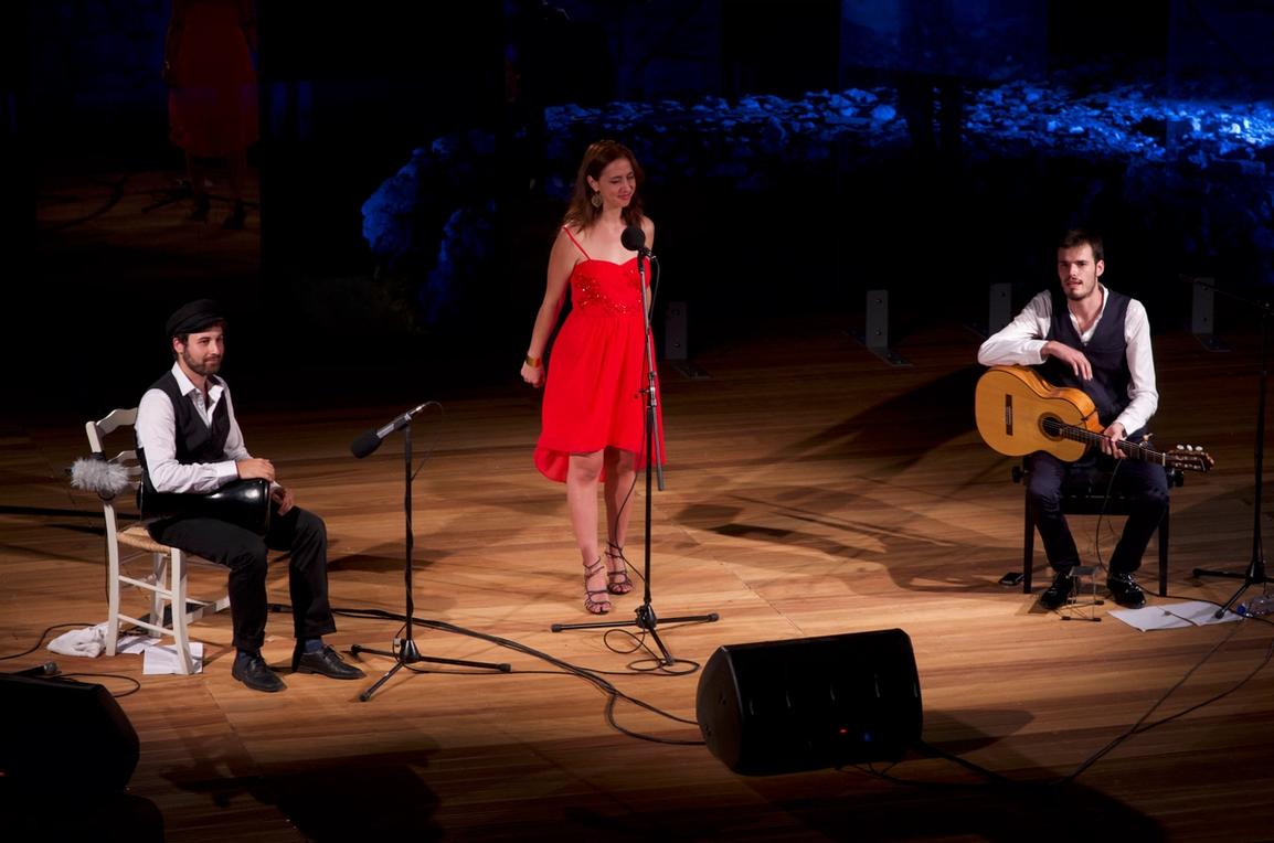 A man playing a drum, a woman singing and a man with a guitar on stage of the Samos Young Artists Festival 2017
