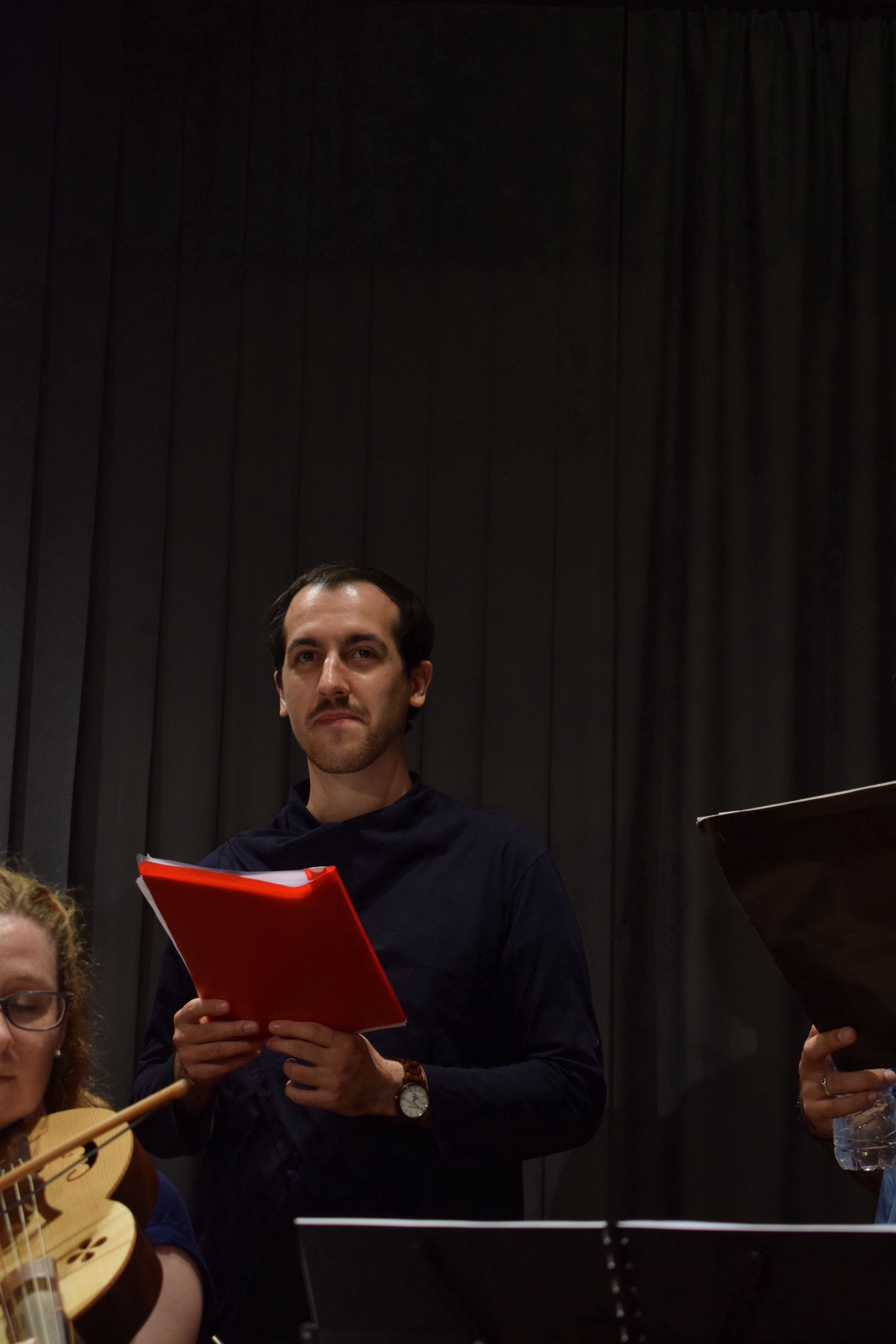 A young man wearing a blue shirt, standing onstage, holding notes. He is a singer