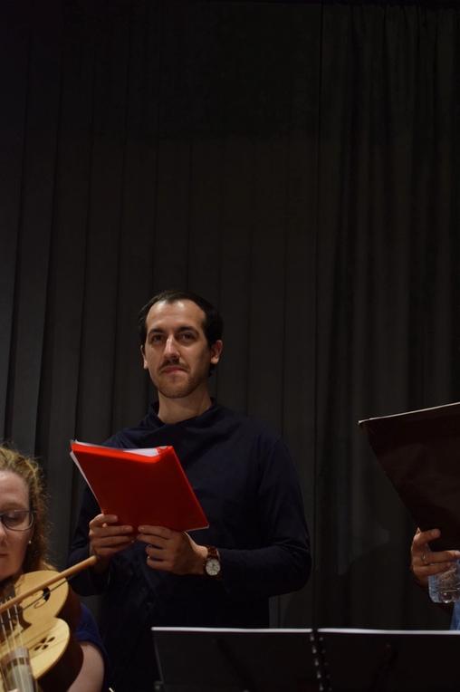 A young man wearing a blue shirt, standing onstage, holding notes. He is a singer