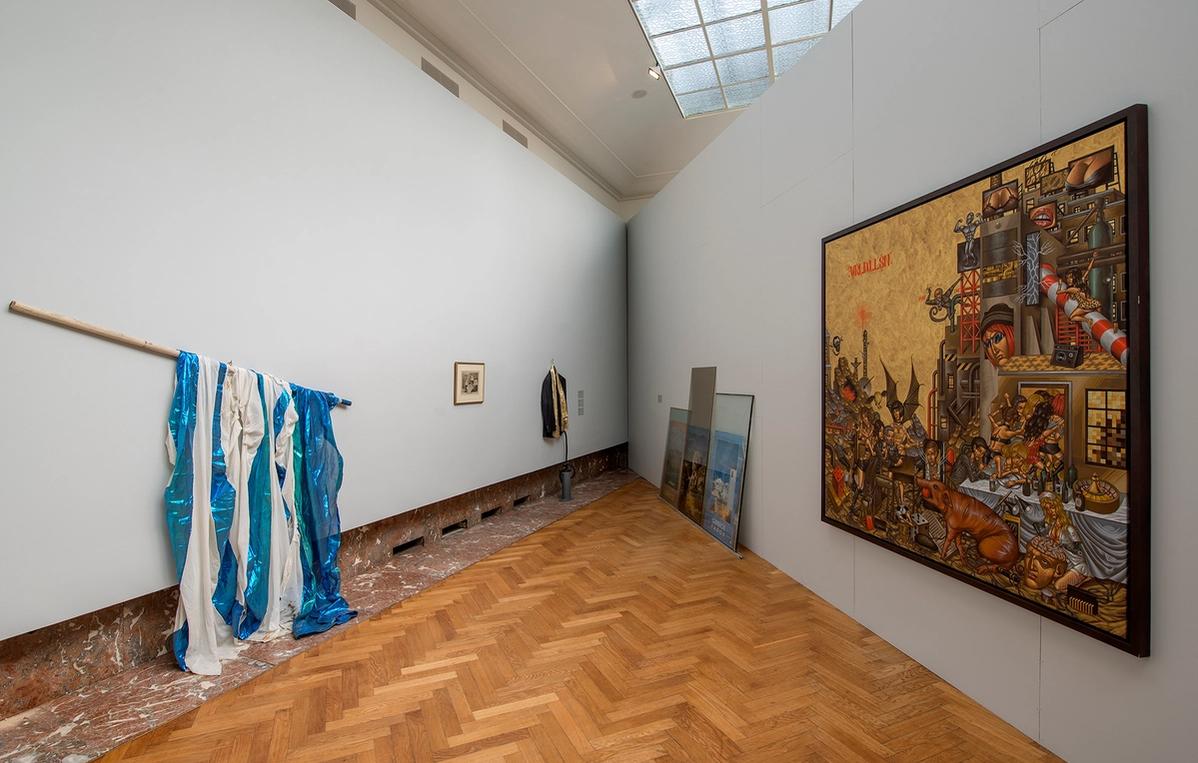 Installation view of an exhibition hall featuring works made out of flagpole and pieces of cloth. To the right a large, framed byzantine-icon-like work hangs on the wall.