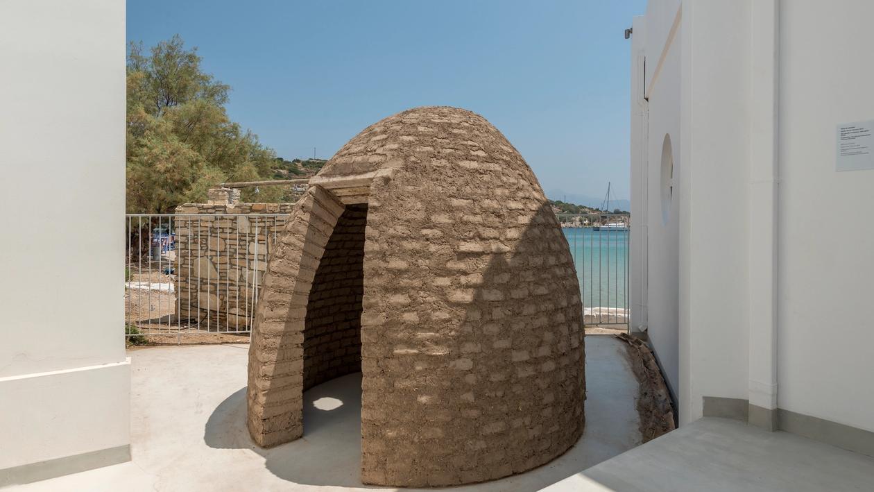 A bee-hive structure, housing example made out of dirt-hay adobe bricks with a single entrance and a small window. Constructed in the art space pythagorion's courtyard only a few meters away from the seafront.