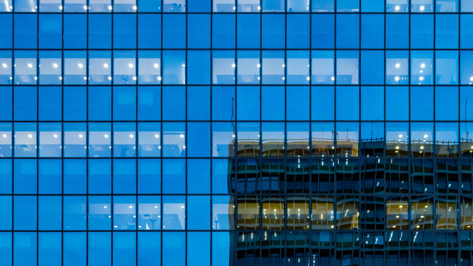 The reflection of an office building on the facade of another total-glass building across. The remaining glass area looks blue from the reflection of the sky.