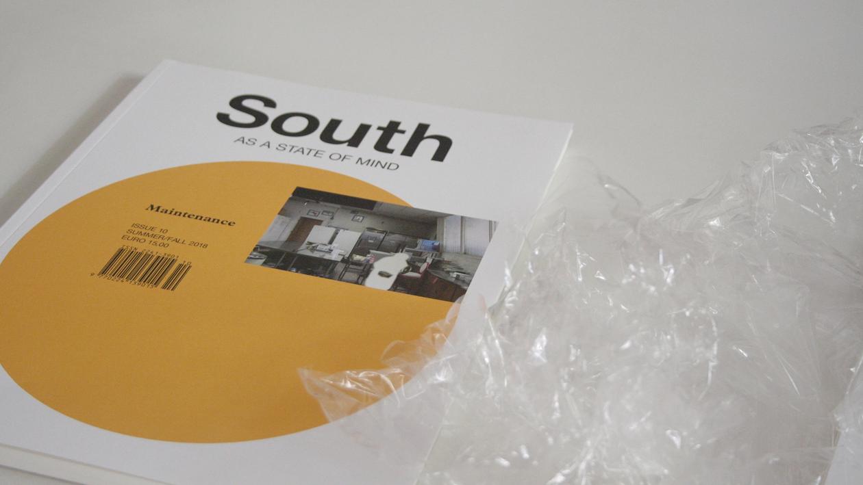 Close up of south as a state of mind magazine. Its plastic wrapping is next to it. 