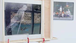 Part of Thu Van Tran's installation depicting a falling statue of Stalin. Reflected on it is the Art Space Pythagorion's view to the open sea and tourists swimming. At the background Georges Salameh picture "Cavafy" is hanged on the wall showing people sitting on a bench.