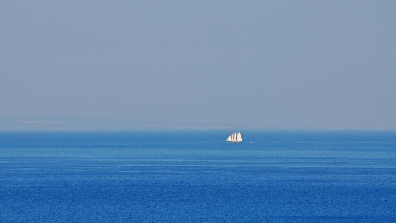 the blue sky and the the blue sea, at the horizon a sailing boat