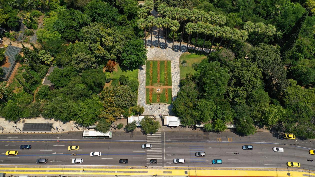 Aerial shot of the National Garden of Athens. The entrance of the garden is situated on a busy central avenue with cars.