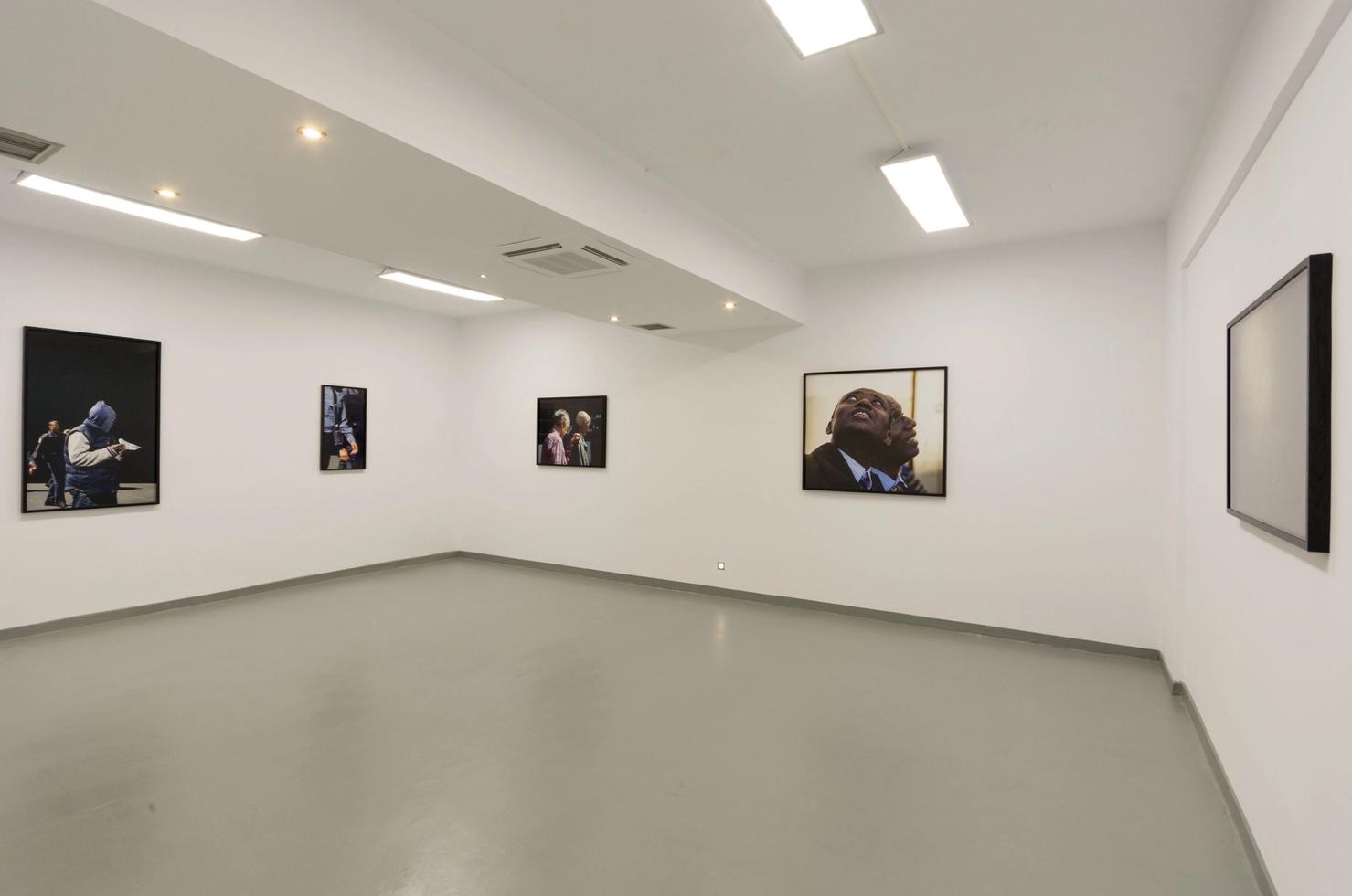 Ein Galeriesaal mit grauem Zementfußboden und weißen Wänden mit gerahmten Bildern.