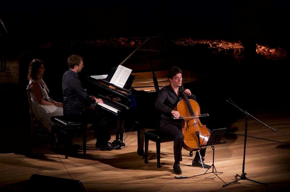 A woman on a chair next to the grand piano played by a pianist and in front a cellist at the stage of the Samos Young Artists Festival 2017