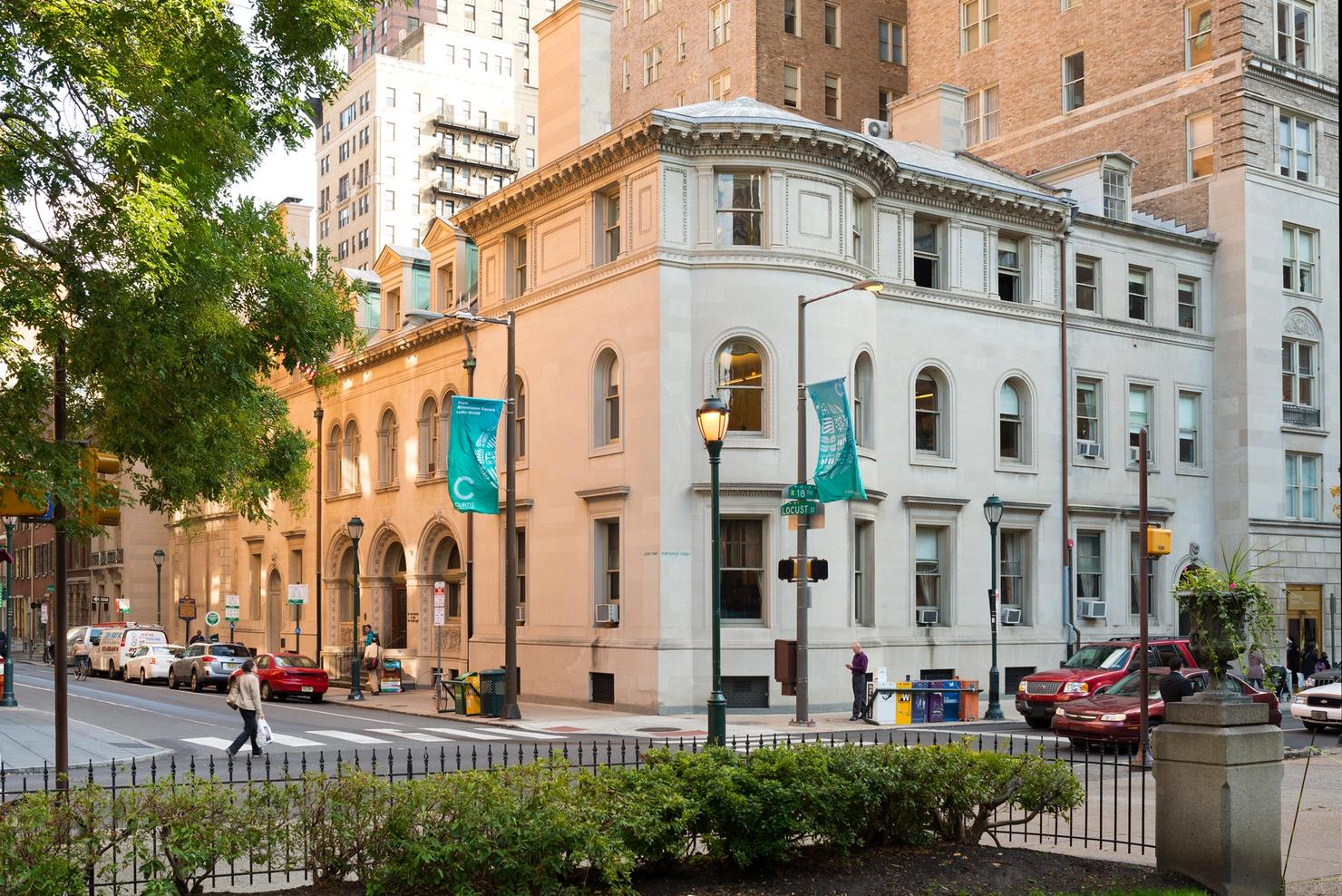 A beige building photographed from the corner of the road with flags of the Curtis Institute in front