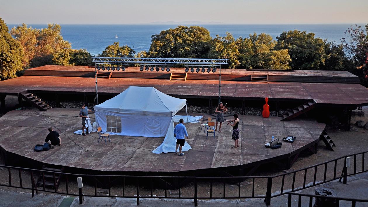 The stage of the Samos Young Artists Festival during the day. Musicians rehearsing and technical staaff working.. In the middle of the stage a white tent protecting the piano from the heat