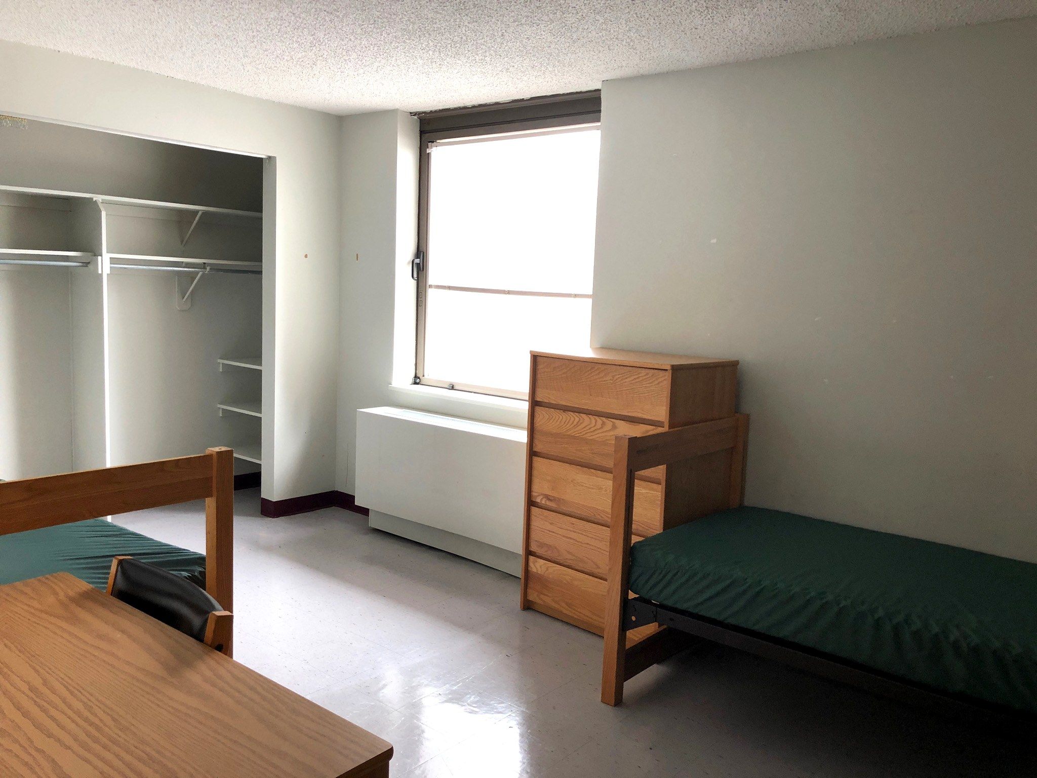 An empty double room at Fordham Lincoln Center with twin beds, desk, dresser and an open closet