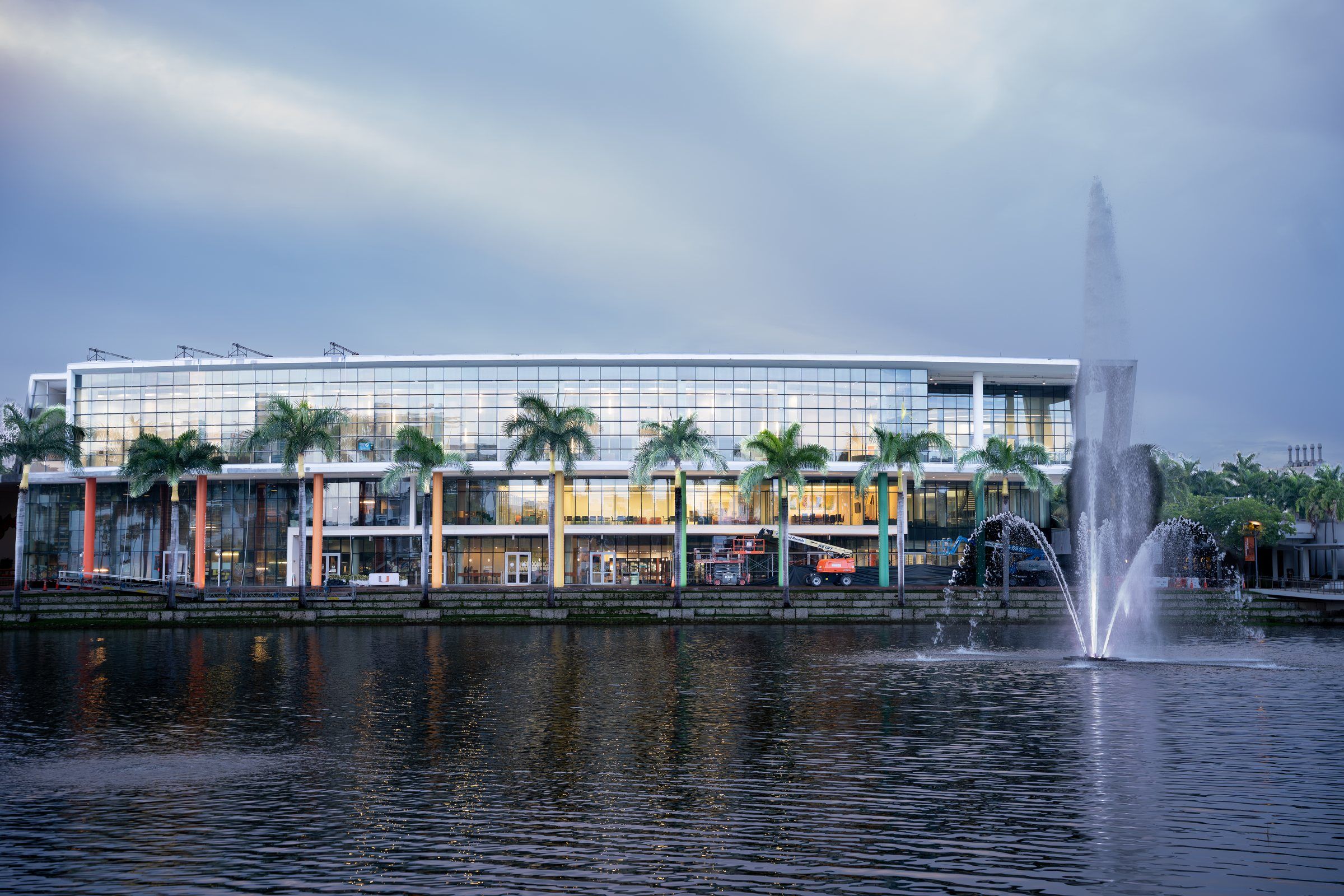Lake Osceola with its fountain and a glass building lined with palms at the University of Miami